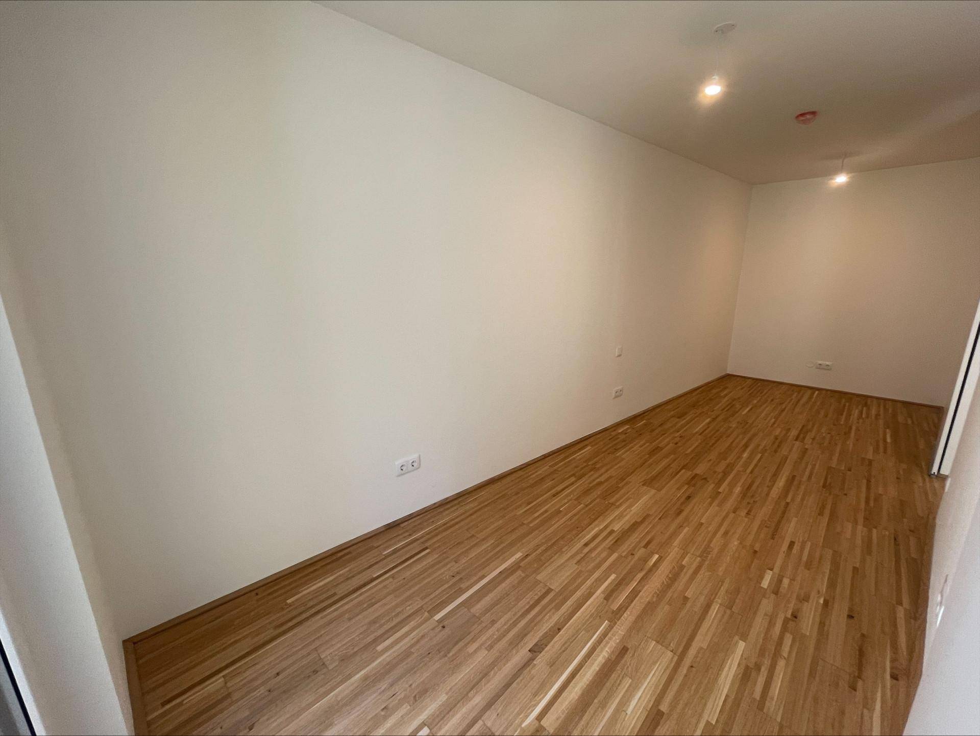 Helles, leeres Zimmer mit Holzboden und weißen Wänden, ideal als Schlafzimmer oder Arbeitszimmer.