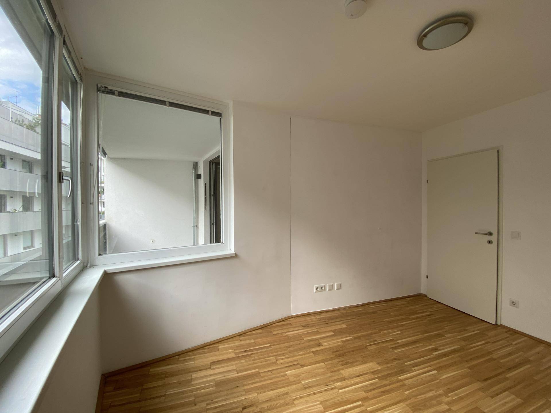 Schlafzimmer mit hellem Parkettboden und großen Fenstern für viel Tageslicht.