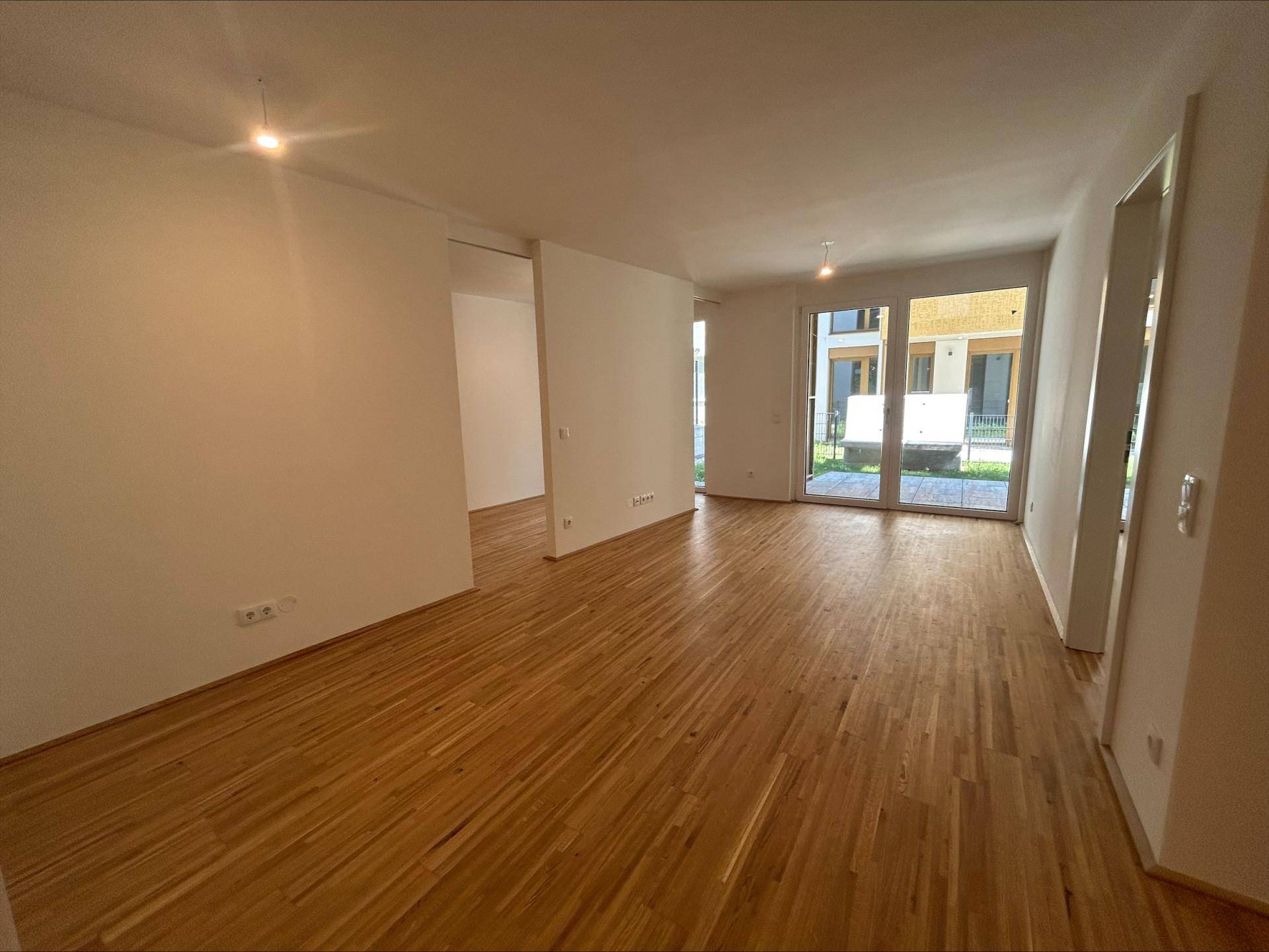 Heller Wohnbereich mit neuem Parkettboden und großen Fenstertüren zum Außenbereich.