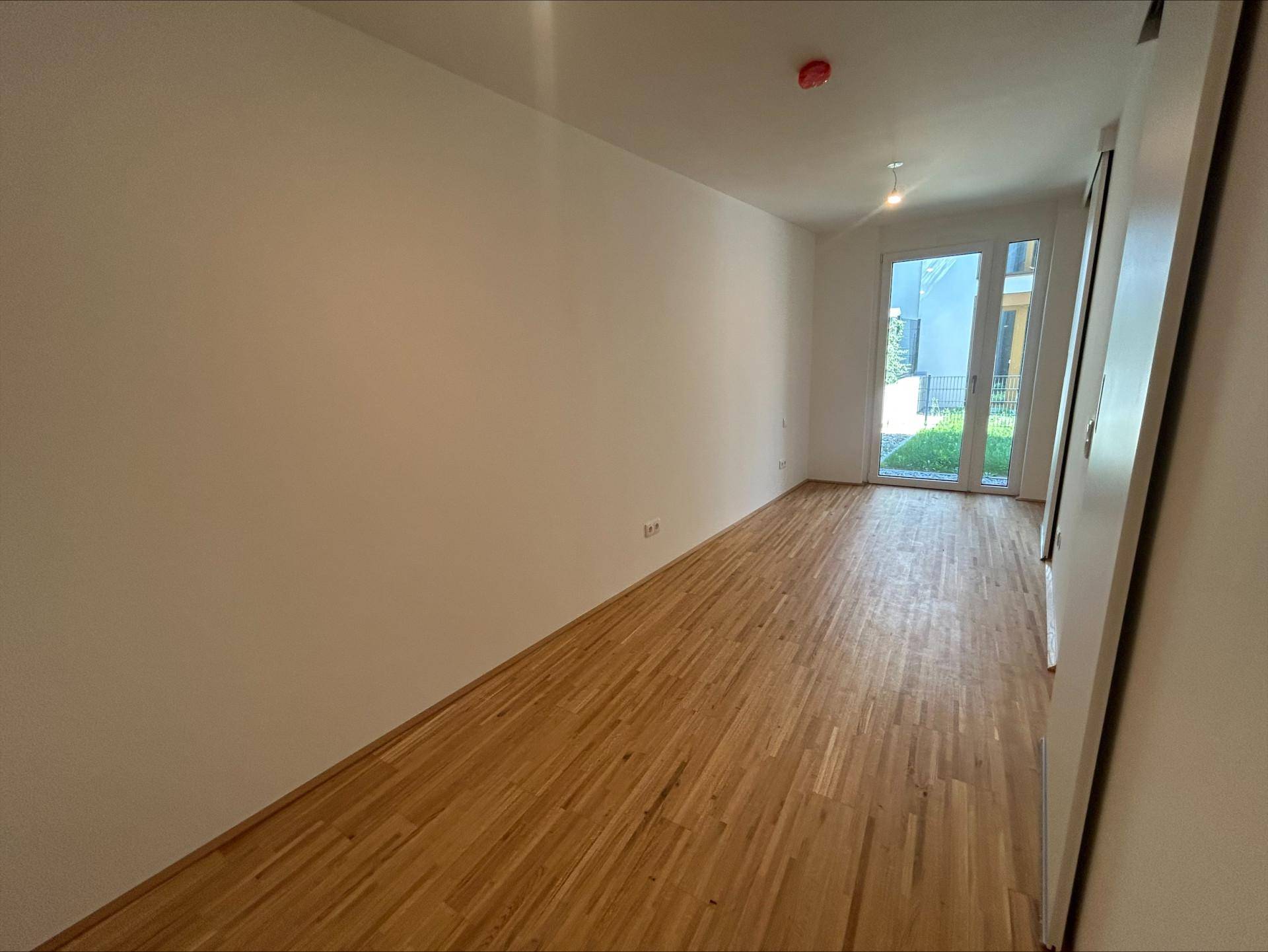 Langes, helles Zimmer mit Parkettboden und Zugang zu einem privaten Außenbereich.