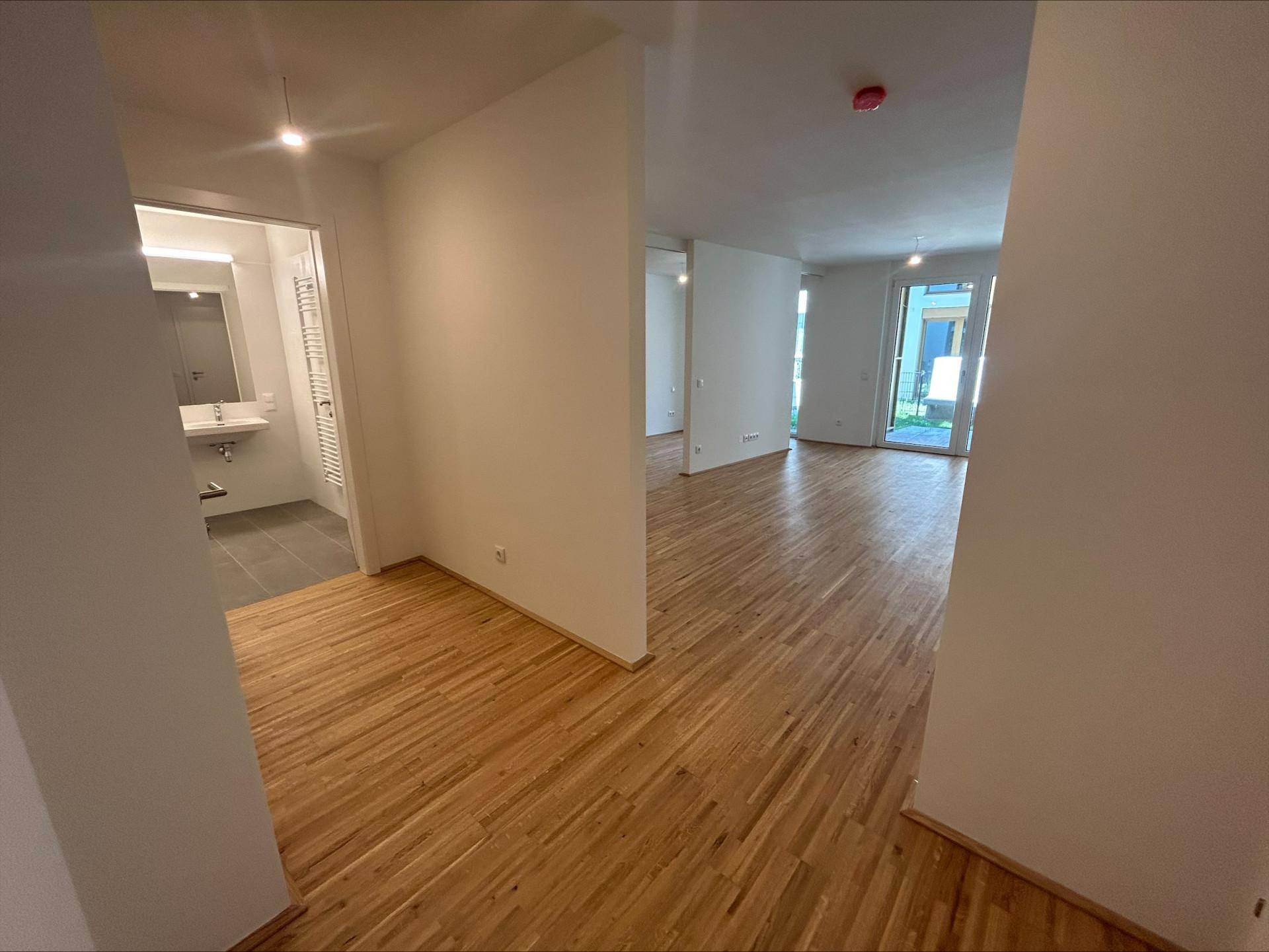 Offener Wohnbereich mit hellem Parkettboden und Zugang zu einem modernen Badezimmer.