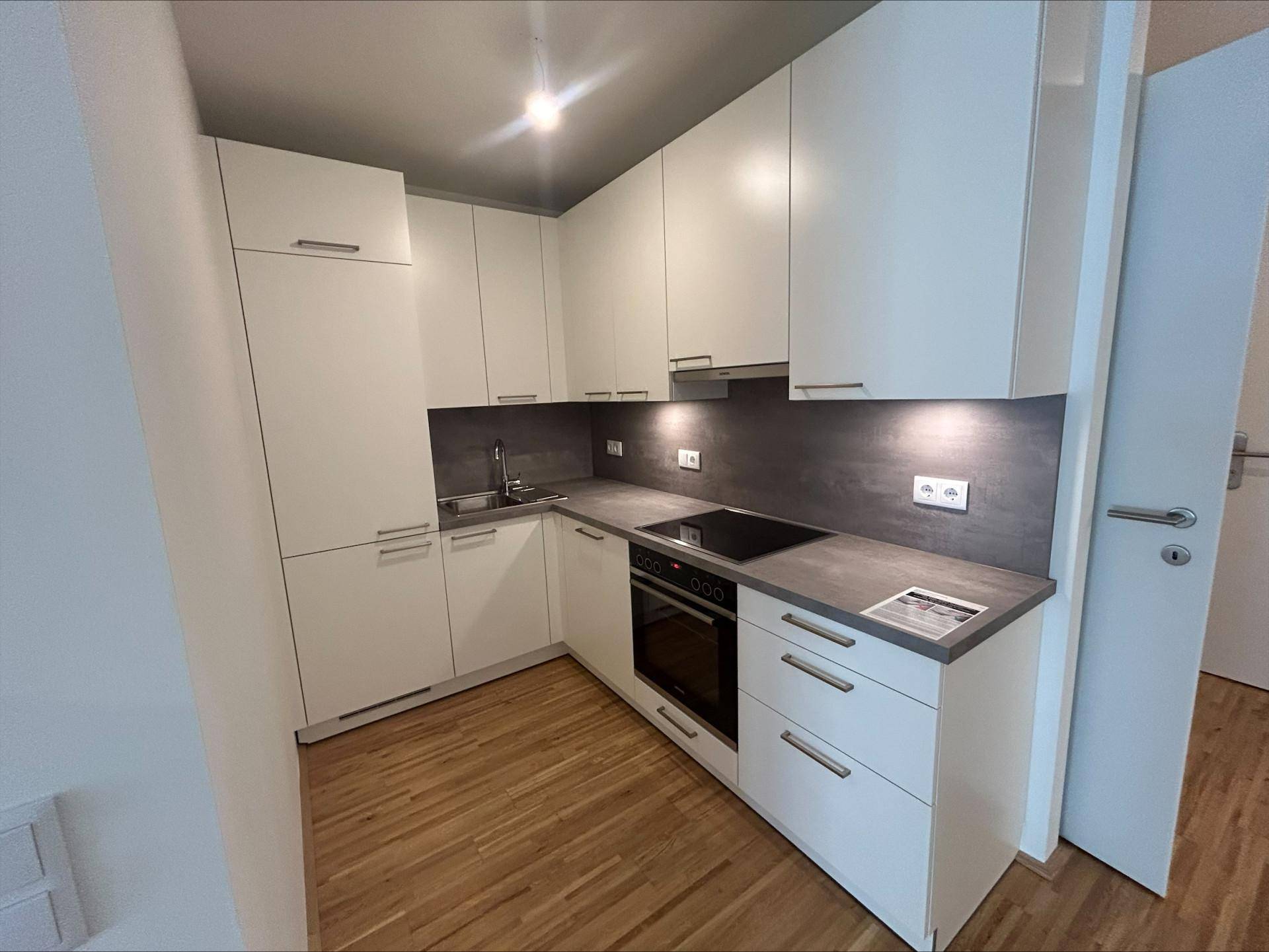 Moderne Einbauküche mit weißen Schränken, dunkler Arbeitsplatte und integrierten Geräten.
