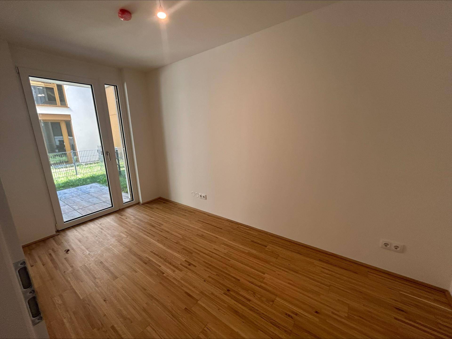 Helles Schlafzimmer mit Holzboden und großen Fenstern, die viel Tageslicht hereinlassen.