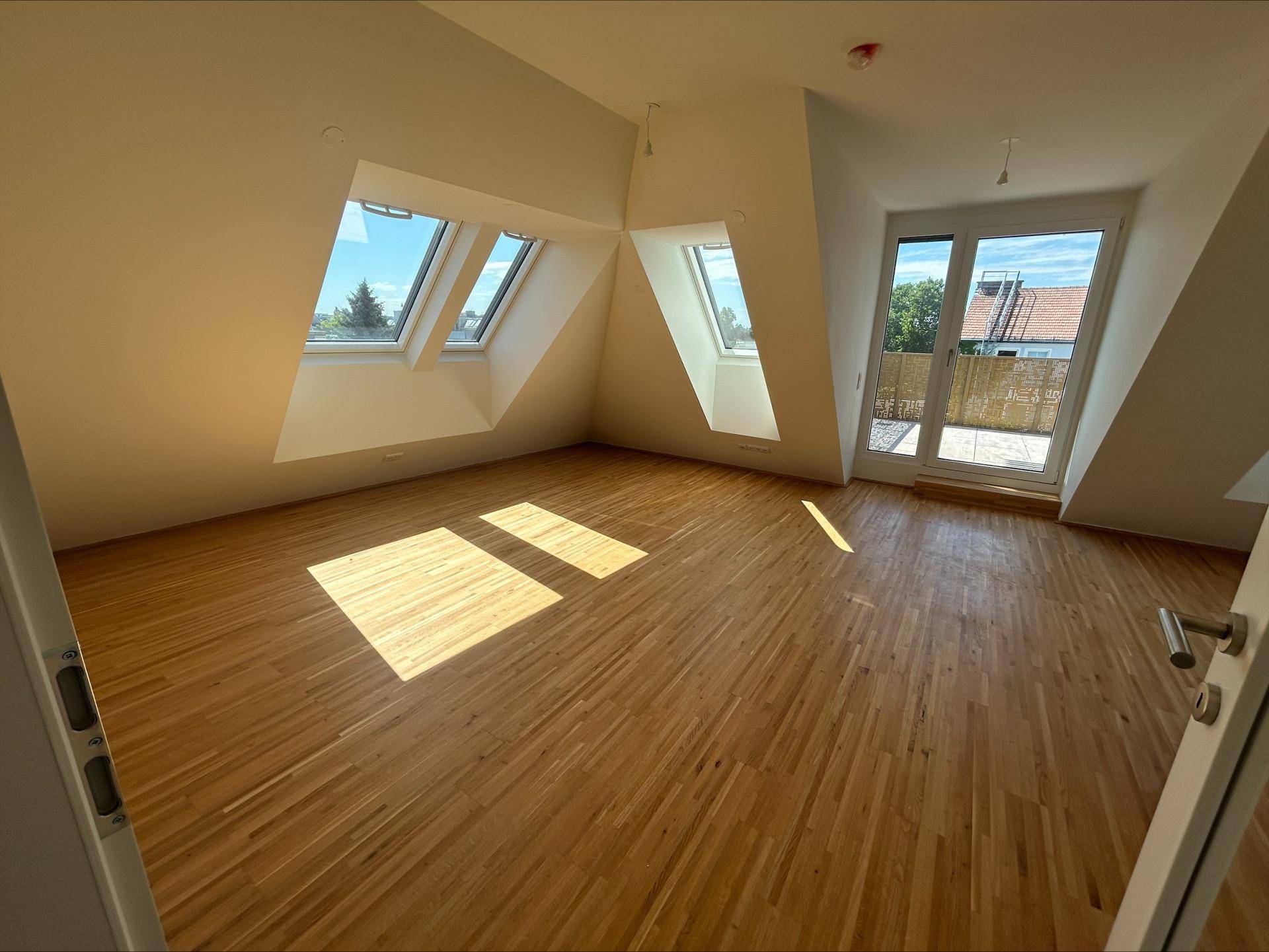 Lichtdurchflutetes Schlafzimmer mit Holzboden, Dachschrägen und Zugang zu einem Außenbereich.