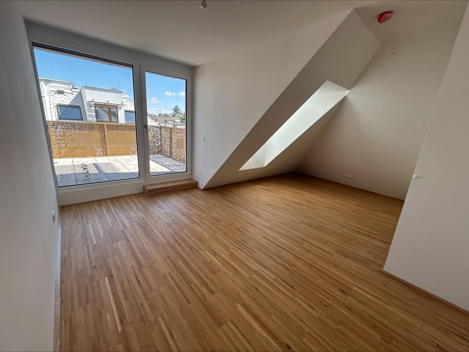 Helles Zimmer mit Holzboden, großen Fenstern und direktem Zugang zur Dachterrasse.