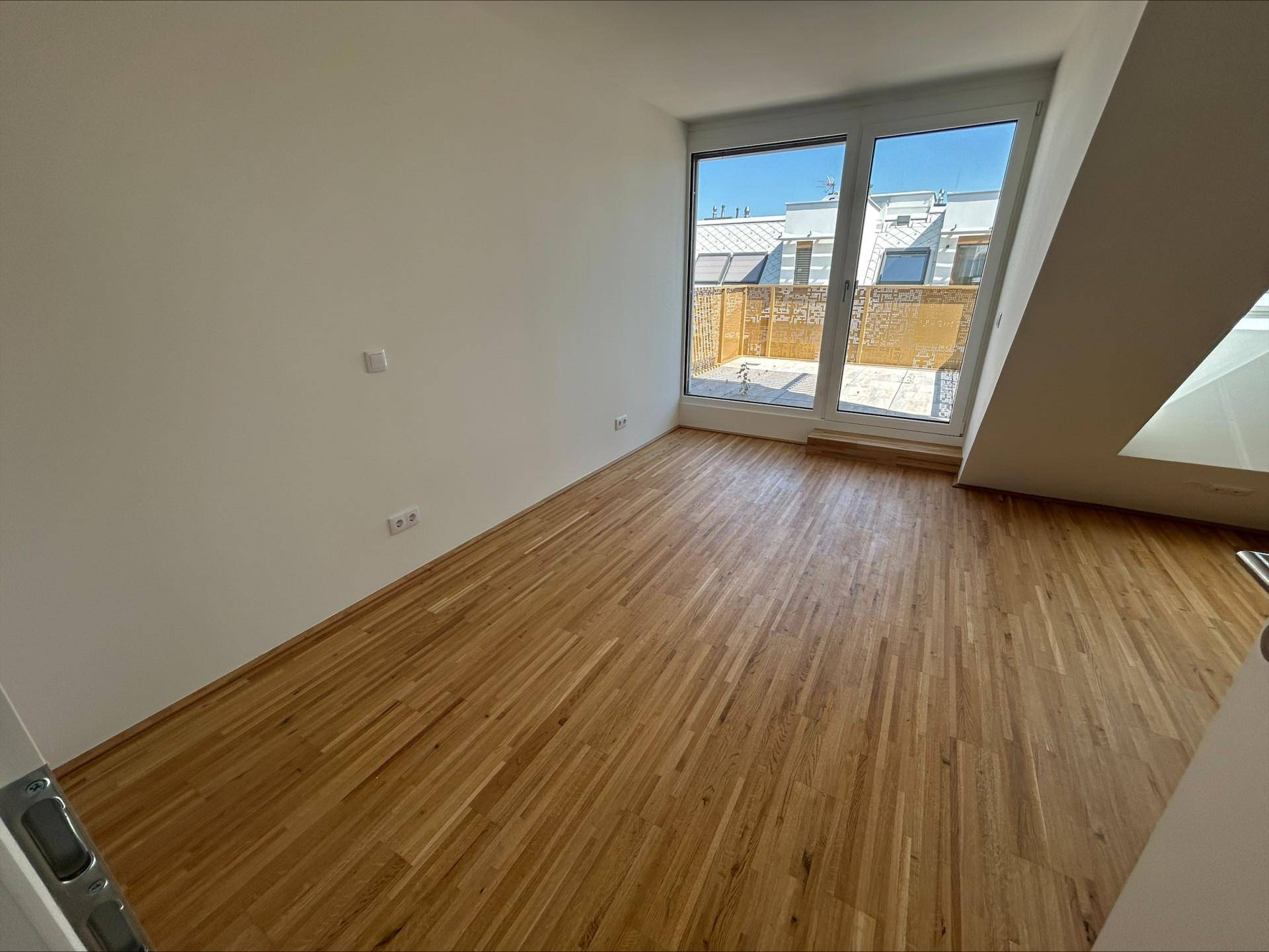 Geräumiges Zimmer mit Holzboden und großen Fenstern, die viel Tageslicht hereinlassen.