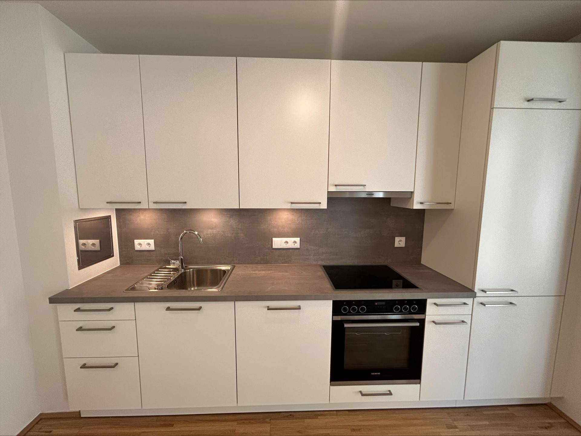 Moderne Einbauküche mit weißen Schränken, integrierten Geräten und dunkler Arbeitsplatte.