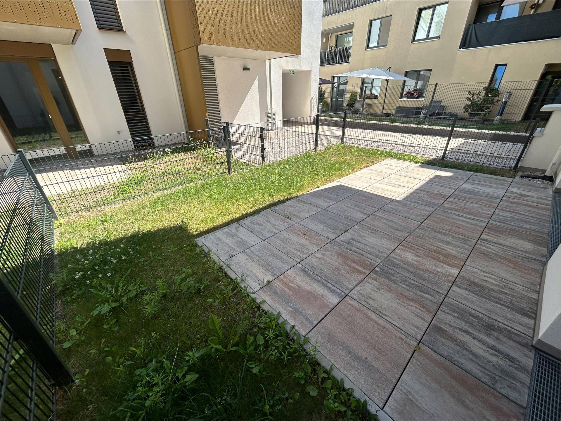 Sonniger Terrassenbereich mit Rasenfläche und Blick auf die umliegenden Gebäude der Wohnanlage.