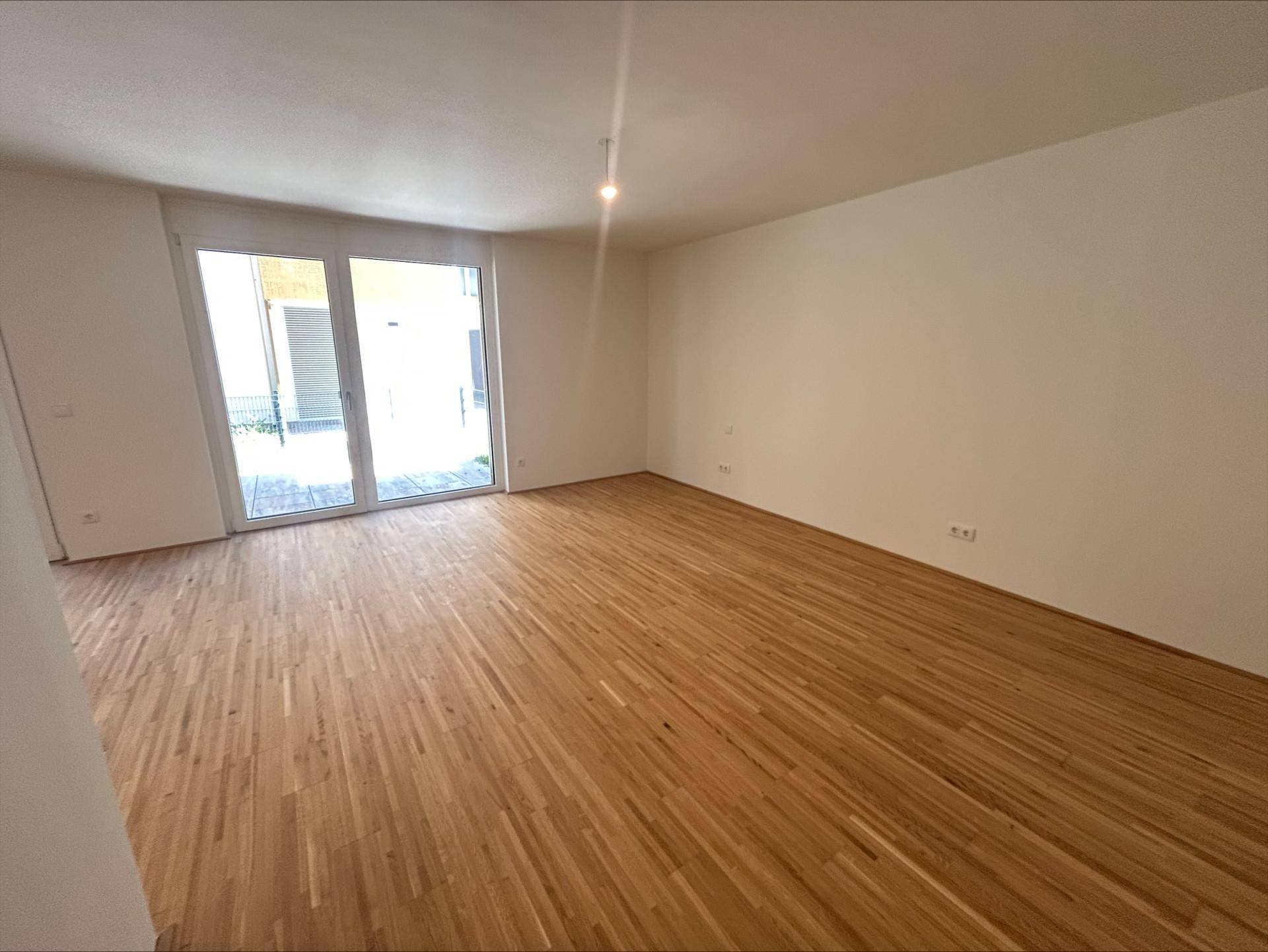 Geräumiger, heller Raum mit Parkettboden und großen Fenstern, die viel Tageslicht hereinlassen.