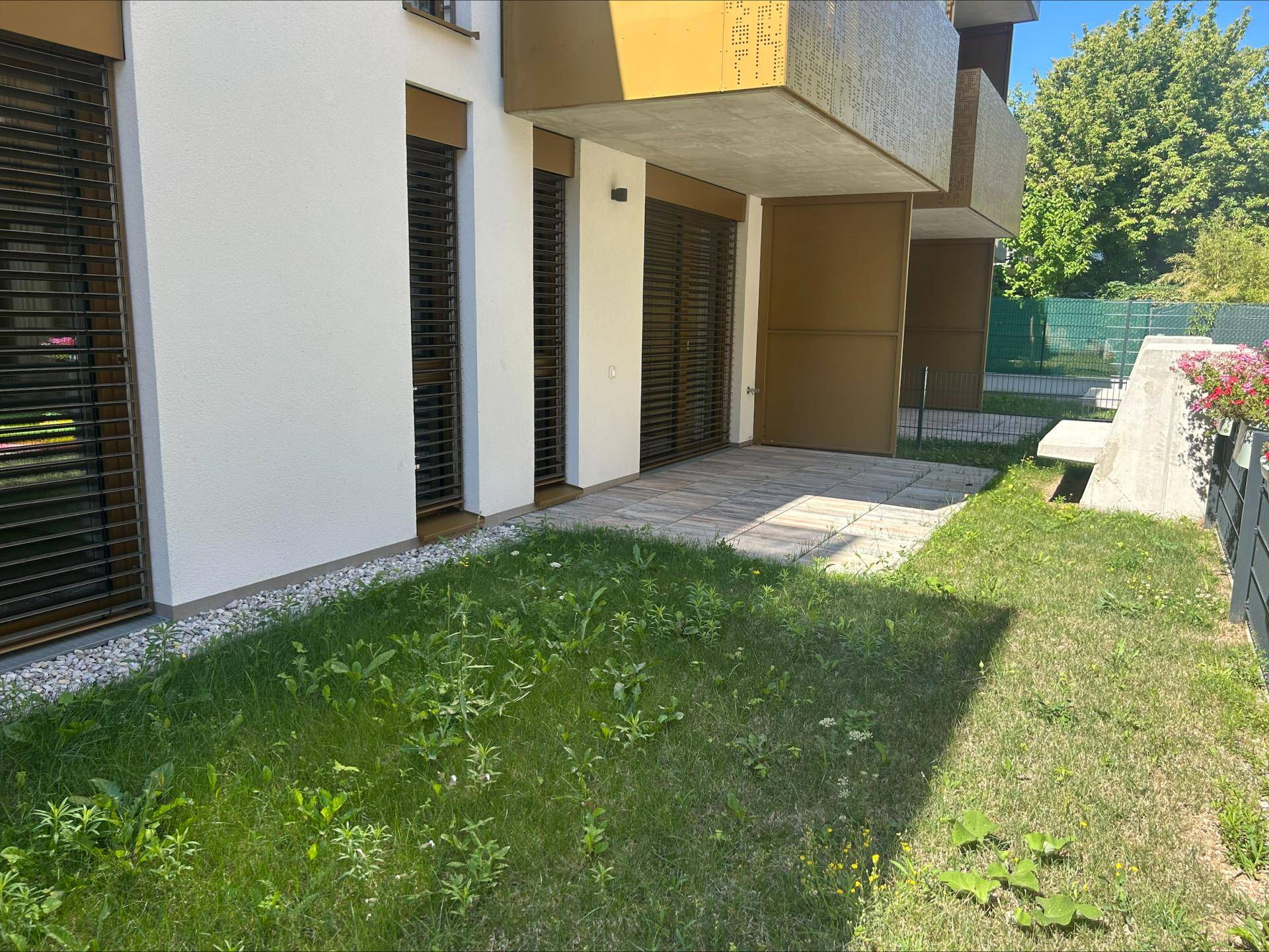 Außenansicht des Gebäudes mit kleiner Rasenfläche und Terrasse, umgeben von grüner Natur.