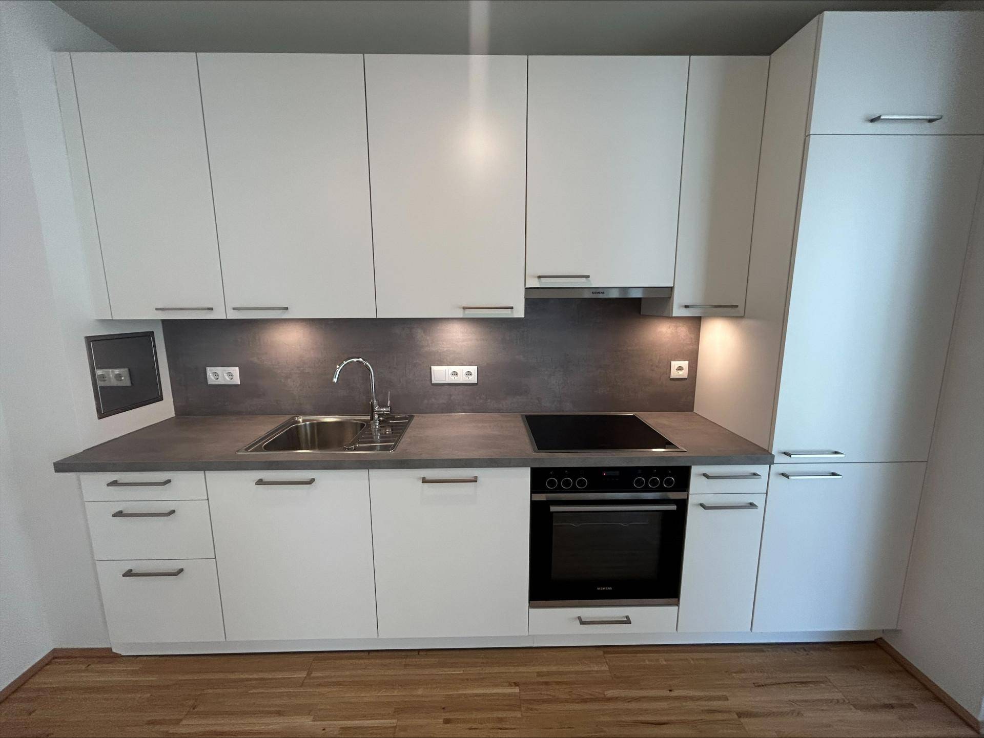 Moderne Einbauküche mit weißen Schränken, Induktionskochfeld und integriertem Backofen.