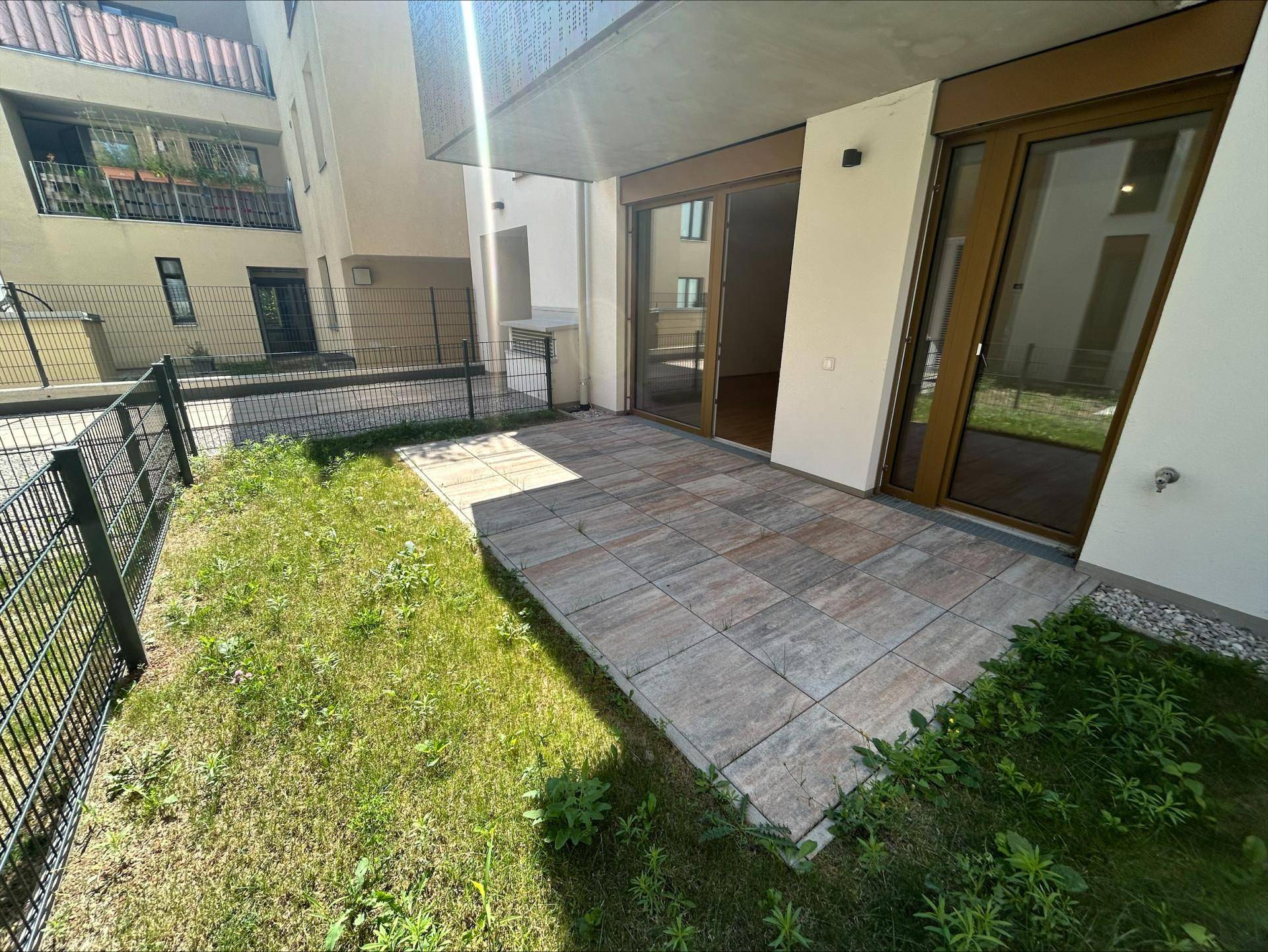 Private Terrasse mit Steinplatten und kleinem Rasenbereich, direkt am Gebäude gelegen.