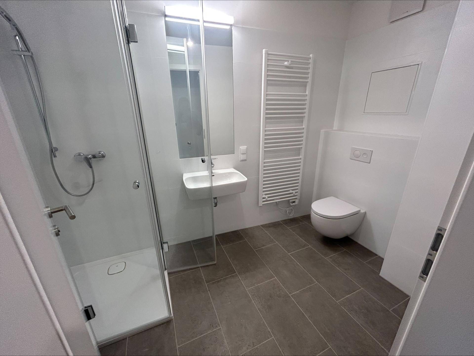 Modernes Badezimmer mit ebenerdiger Dusche, wandhängendem WC und beheiztem Handtuchhalter.
