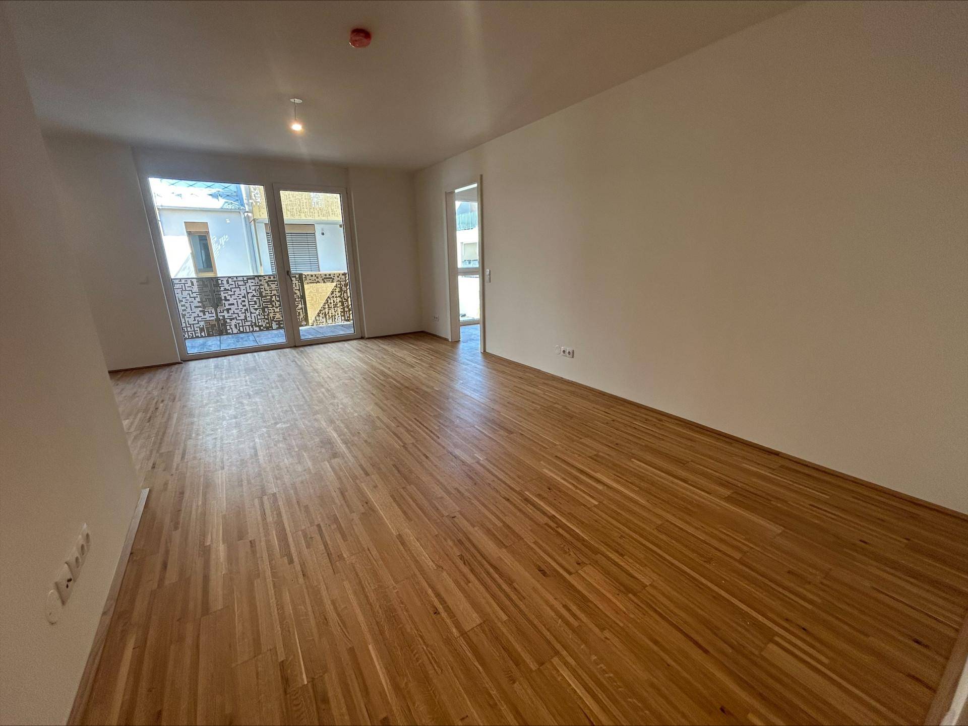 Geräumiges Wohnzimmer mit Holzboden und Zugang zu einem sonnigen Balkon.