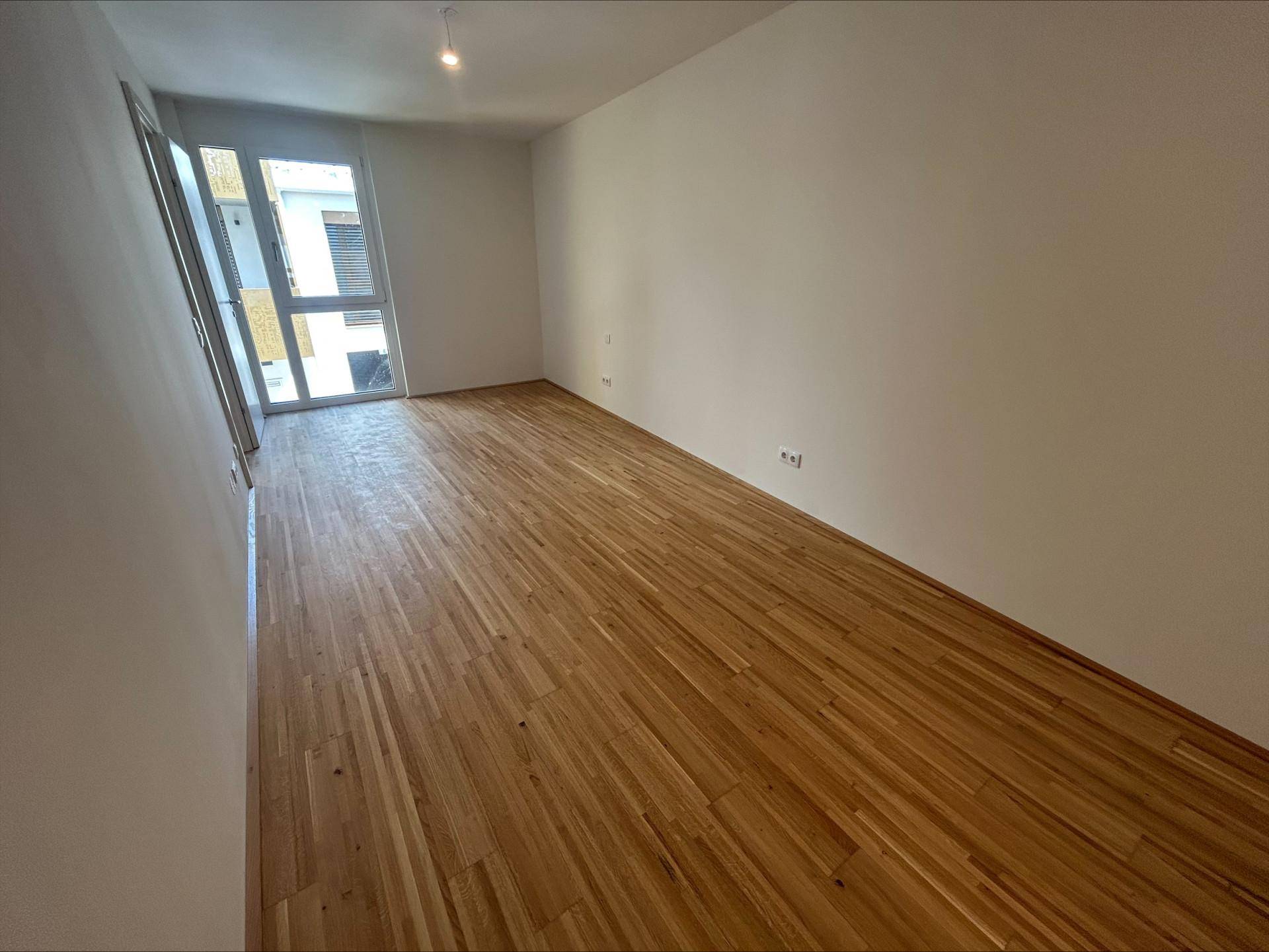 Helles Zimmer mit Holzboden und großem Fenster, ideal als Schlaf- oder Arbeitszimmer.