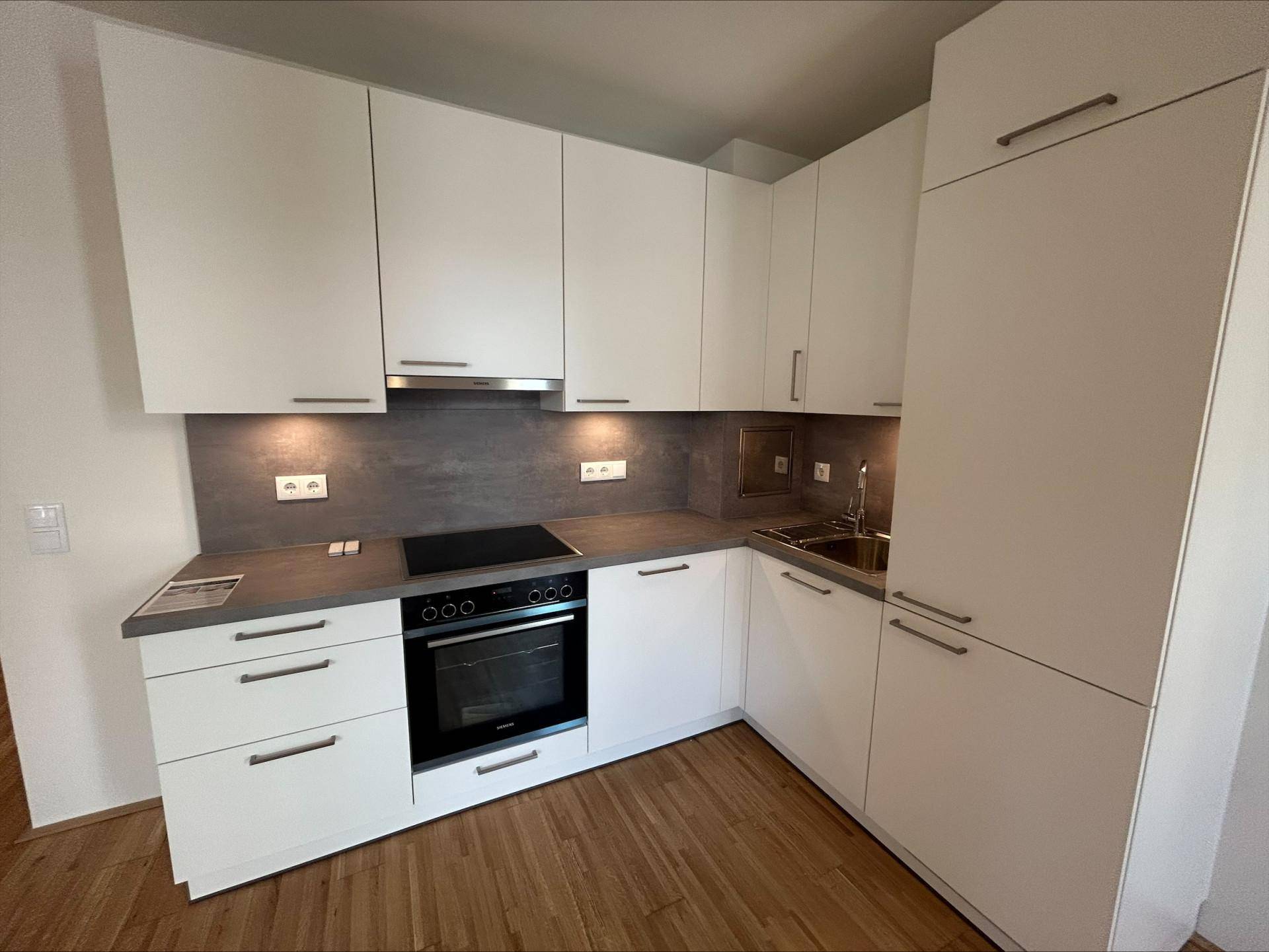 Moderne Einbauküche mit weißen Schränken, dunkler Arbeitsplatte und integrierten Geräten.