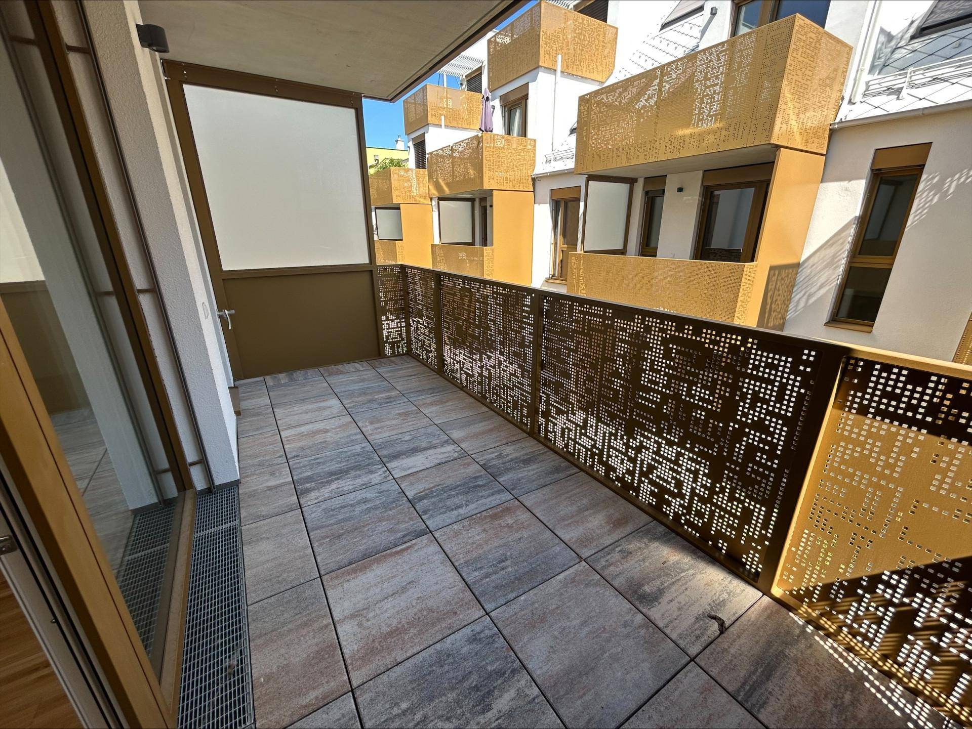 Moderner Balkon mit Fliesenboden und dekorativem Metallgeländer, sonnig gelegen.