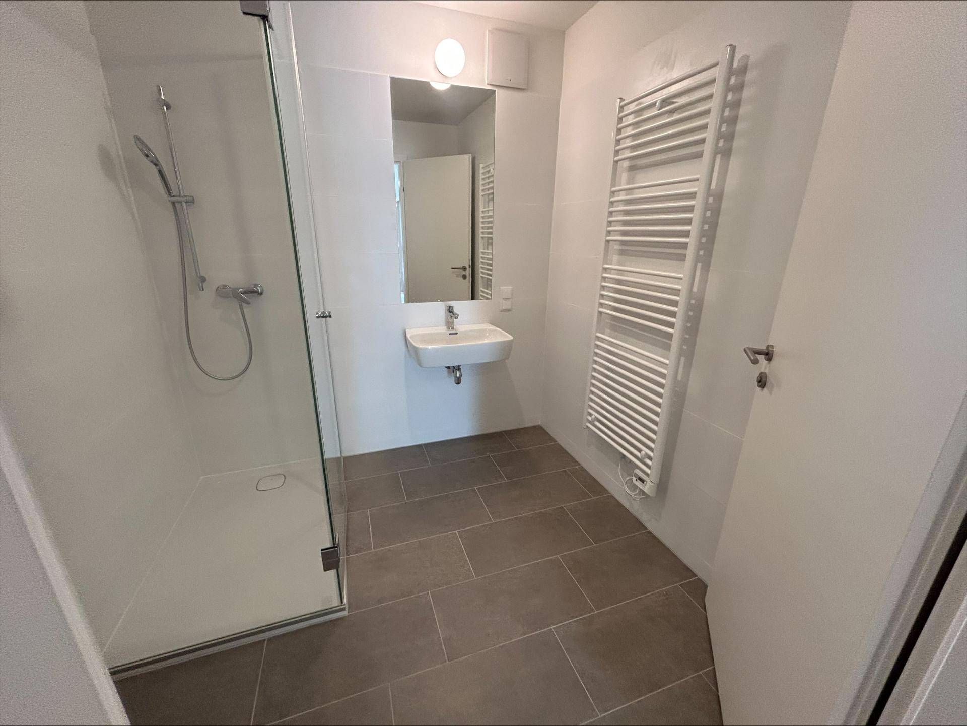 Modernes Badezimmer mit ebenerdiger Dusche, Handtuchheizkörper und hellen Fliesen.