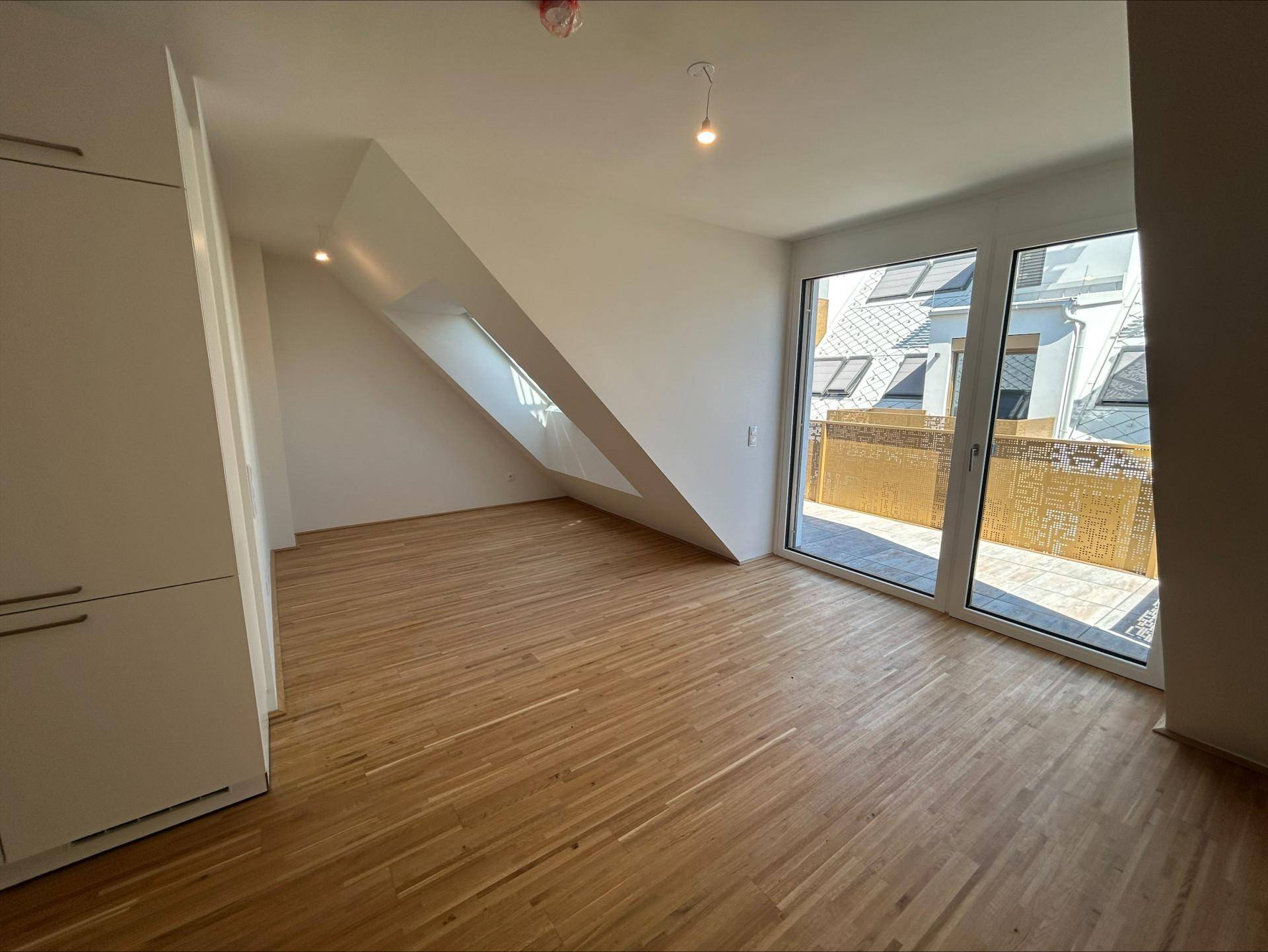 Heller Wohnbereich mit Holzboden, Dachschrägen und großen Fenstern, die auf eine Terrasse führen.