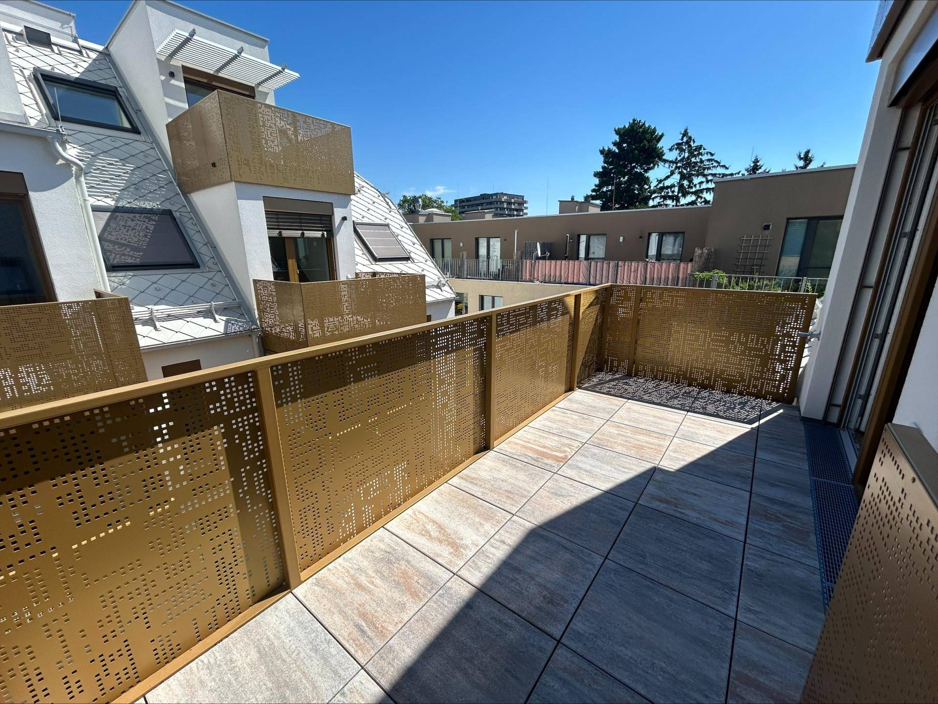 Geräumige Terrasse mit modernen Fliesen und perforierten Metallgeländern unter blauem Himmel.