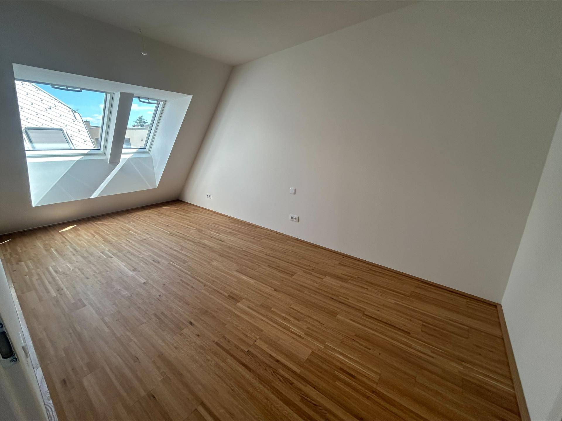 Helles Zimmer mit Holzboden, Dachschrägen und einem großen Dachfenster für viel Tageslicht.