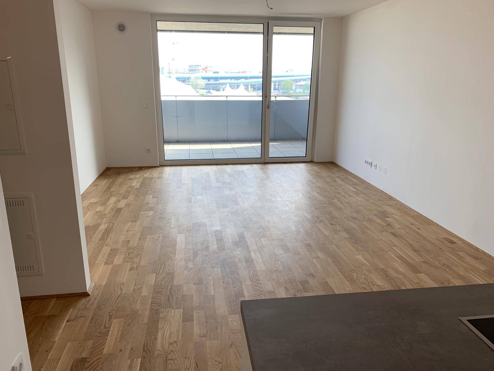 Heller Wohnbereich mit Holzboden und Zugang zu einem Balkon, bietet viel natürliches Licht.