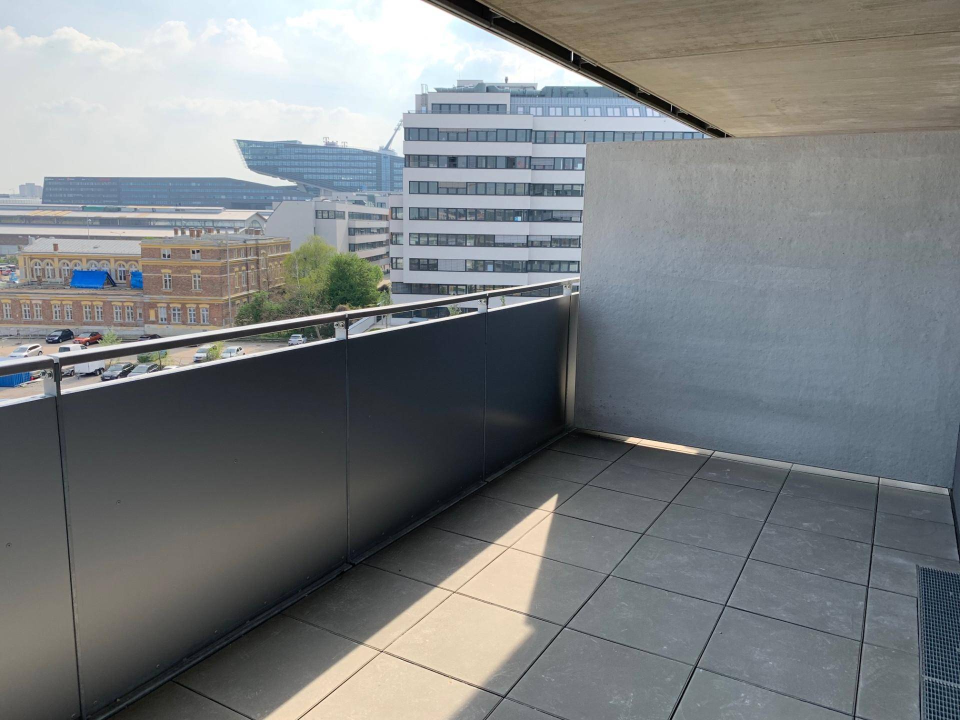 Sonniger Balkon mit Fliesenboden und urbanem Ausblick auf moderne Gebäude.