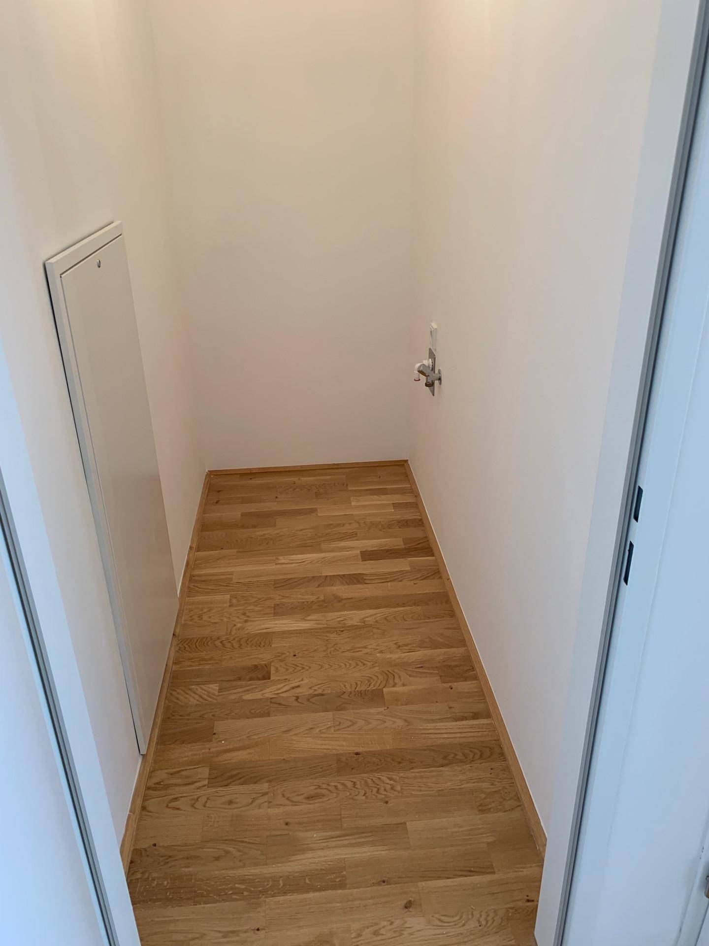 Praktischer Abstellraum mit Holzboden und Anschlüssen für Waschmaschine oder Trockner.