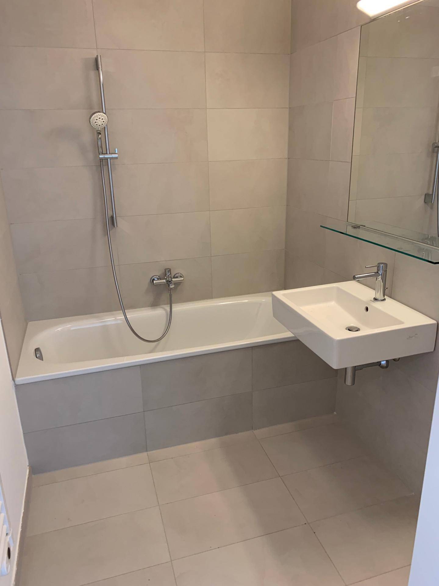 Modernes Badezimmer mit Badewanne, Waschbecken und hellen Fliesen an Wänden und Boden.