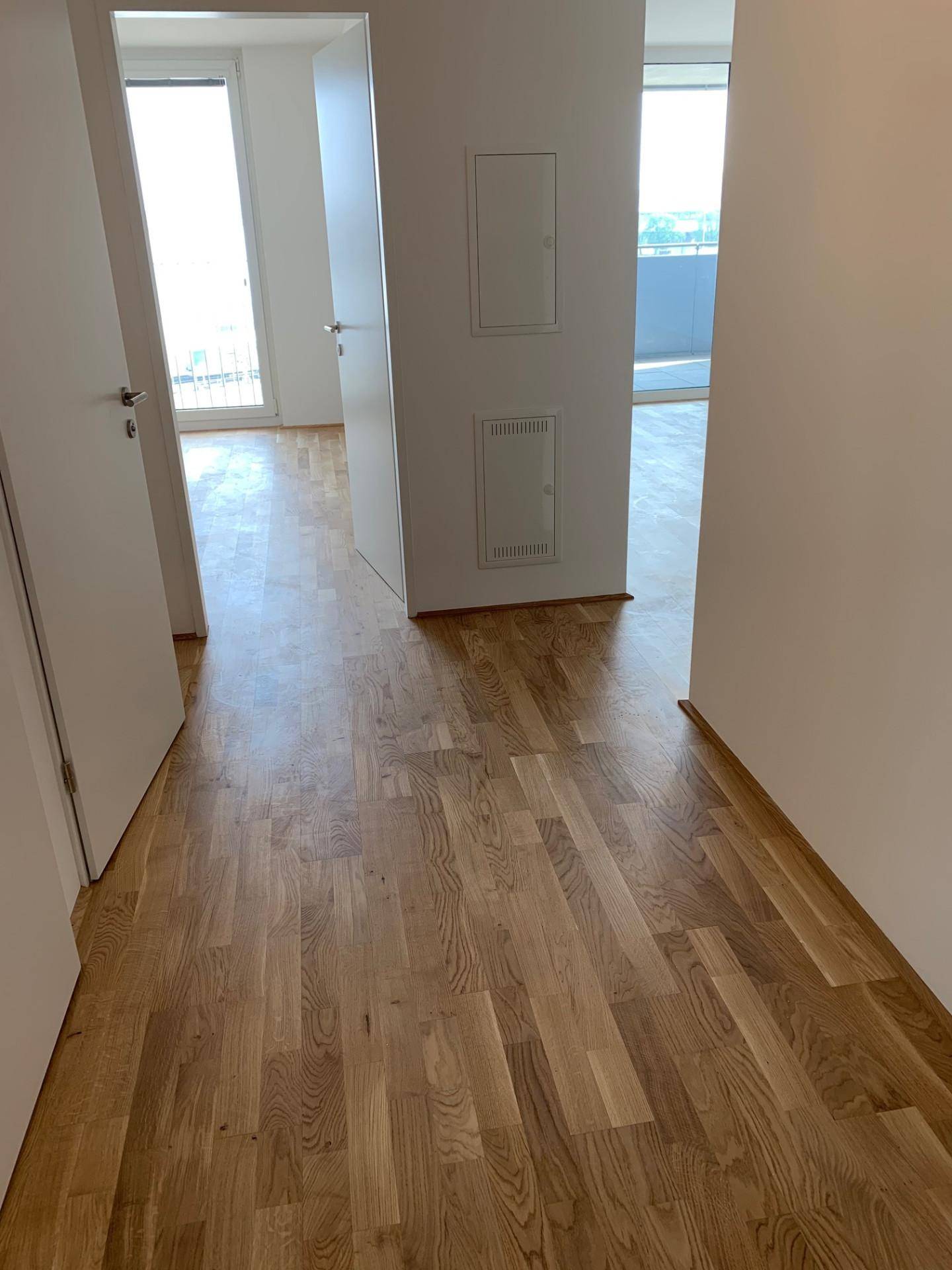 Heller Flur mit Holzboden, der zu verschiedenen Räumen der Wohnung führt.