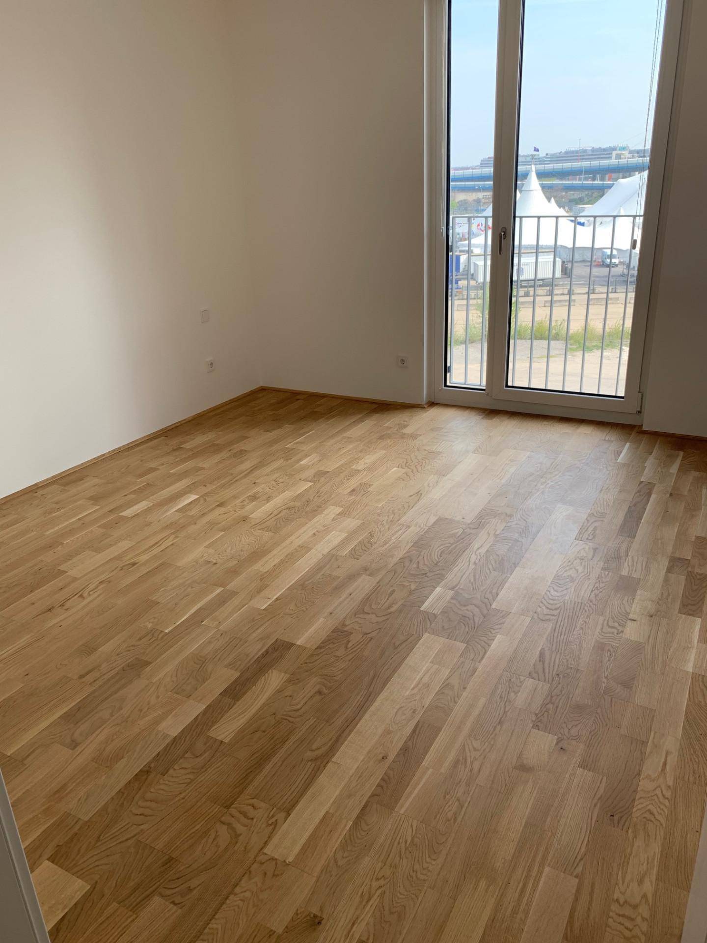 Schlafzimmer mit Holzboden und Zugang zu einem Balkon, bietet viel Tageslicht.