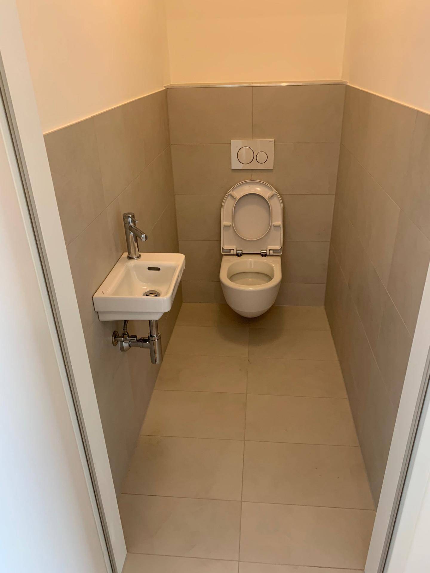 Separates Gäste-WC mit wandhängender Toilette, kleinem Waschbecken und hellen Fliesen.