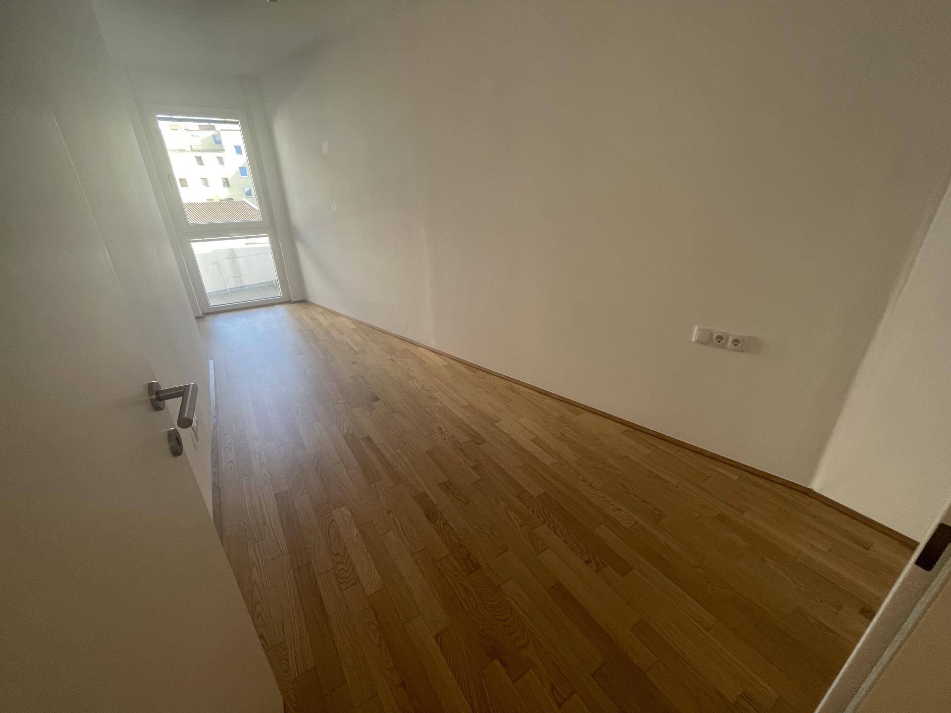 Leerer Raum mit Holzboden und großem Fenster, bereit zur individuellen Gestaltung.