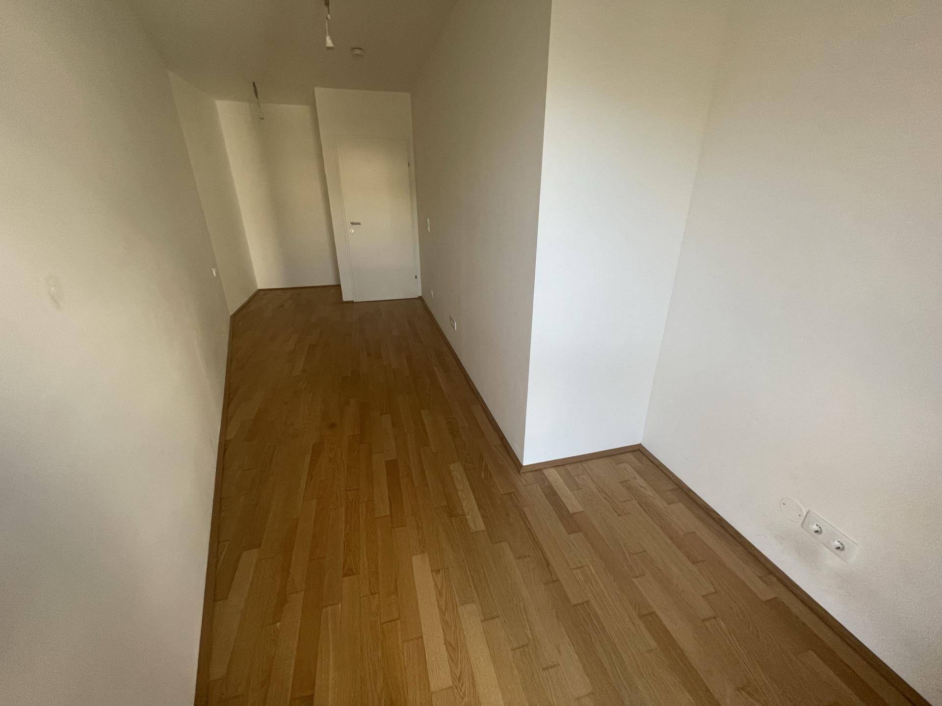 Leerer Raum mit Holzboden und weiß gestrichenen Wänden, vielseitig nutzbar.