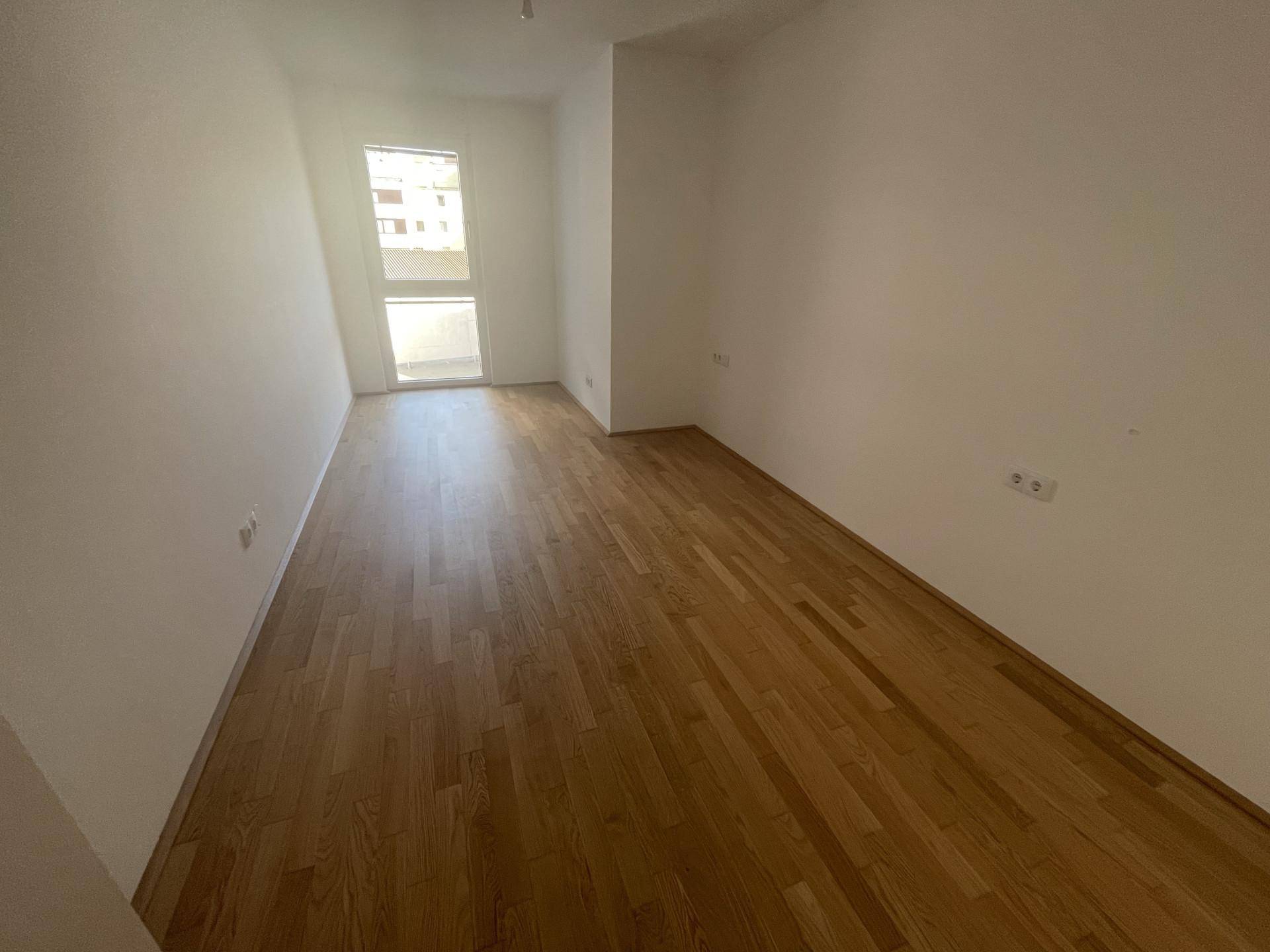 Leerer Raum mit Holzboden und Fenster, bietet viel Tageslicht.