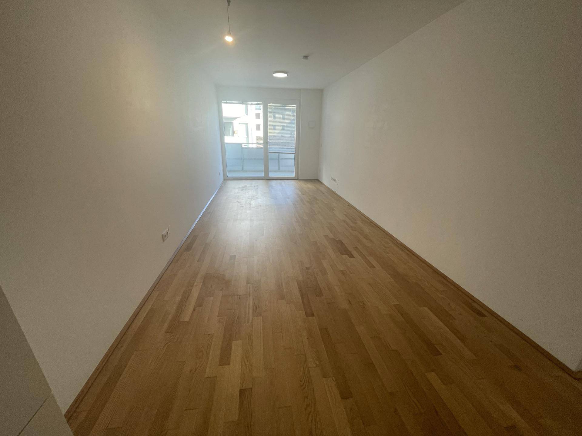 Geräumiger, leerer Raum mit Holzboden und großen Fenstern, ideal für Wohnbereich.