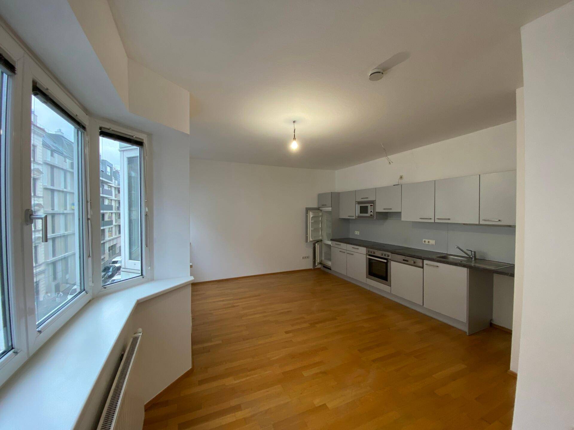 Offener Wohnbereich mit Einbauküche, Parkettboden und breiter Fensterfront.