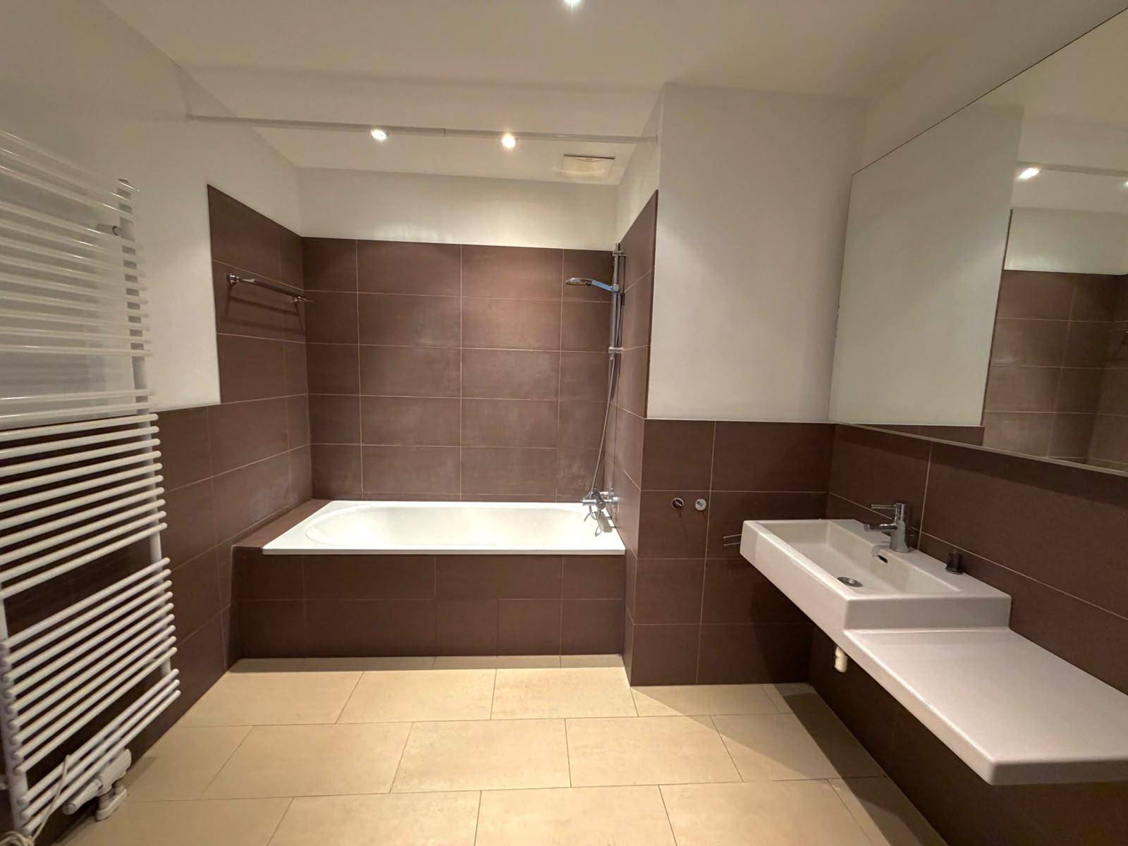 Modernes Badezimmer mit Badewanne, Dusche, Waschtisch und beheiztem Handtuchhalter, elegant gefliest.