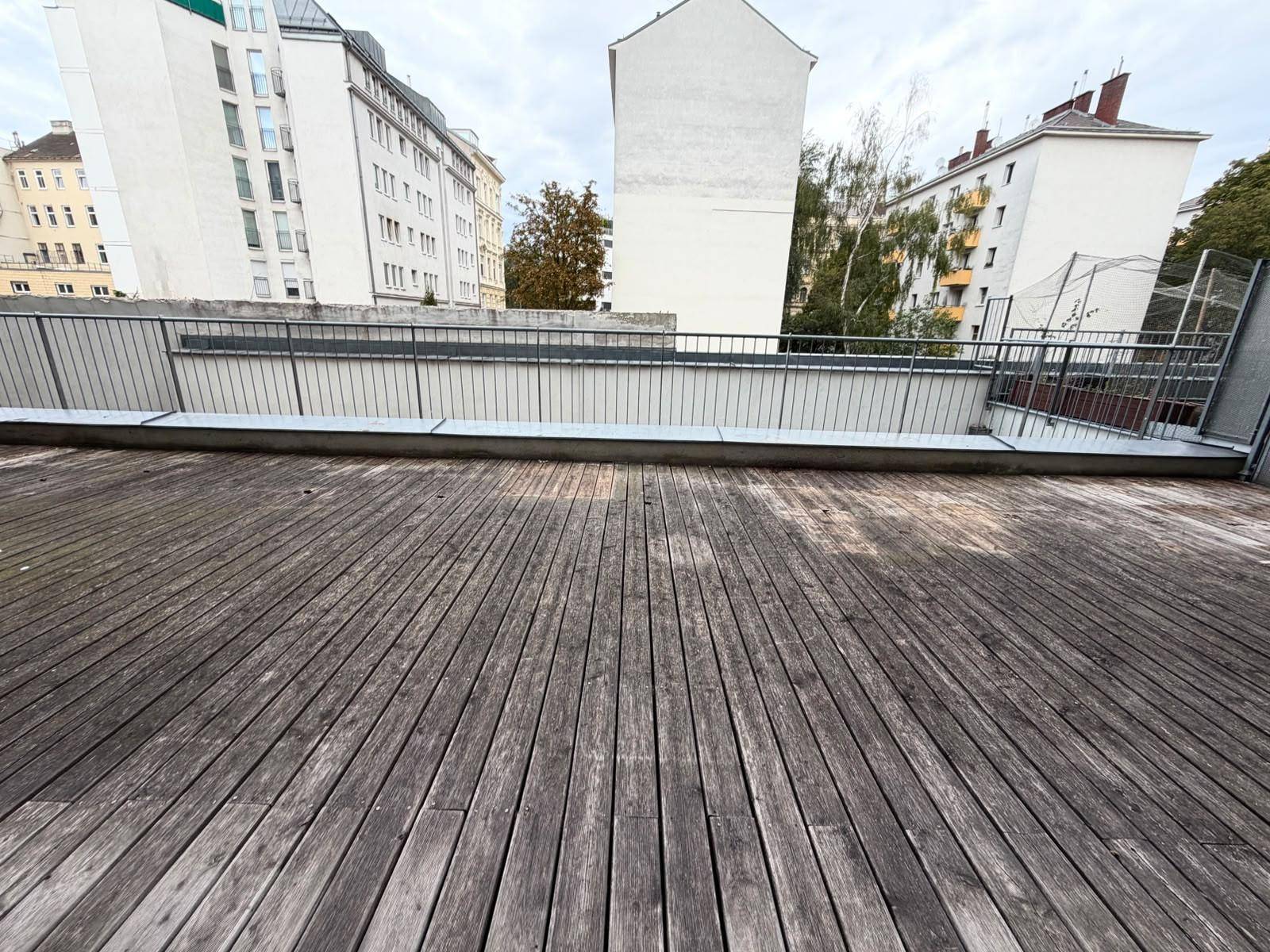 Weitläufige Holzterrasse mit Blick auf die umliegenden Gebäude und den Himmel, ideal zum Entspannen.