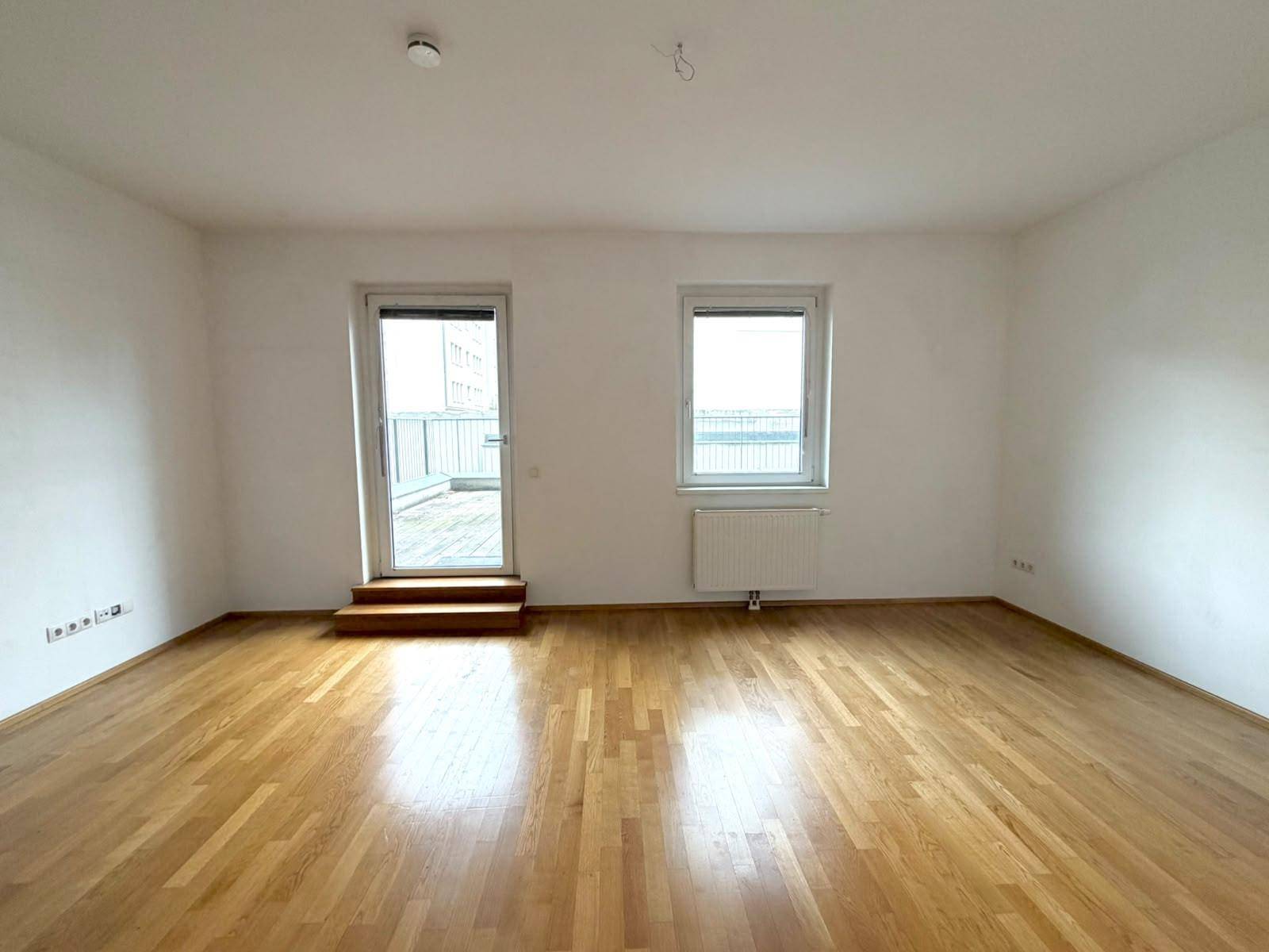 Geräumiges Wohnzimmer mit hellem Parkettboden und direktem Zugang zur Außenterrasse, lichtdurchflutet.