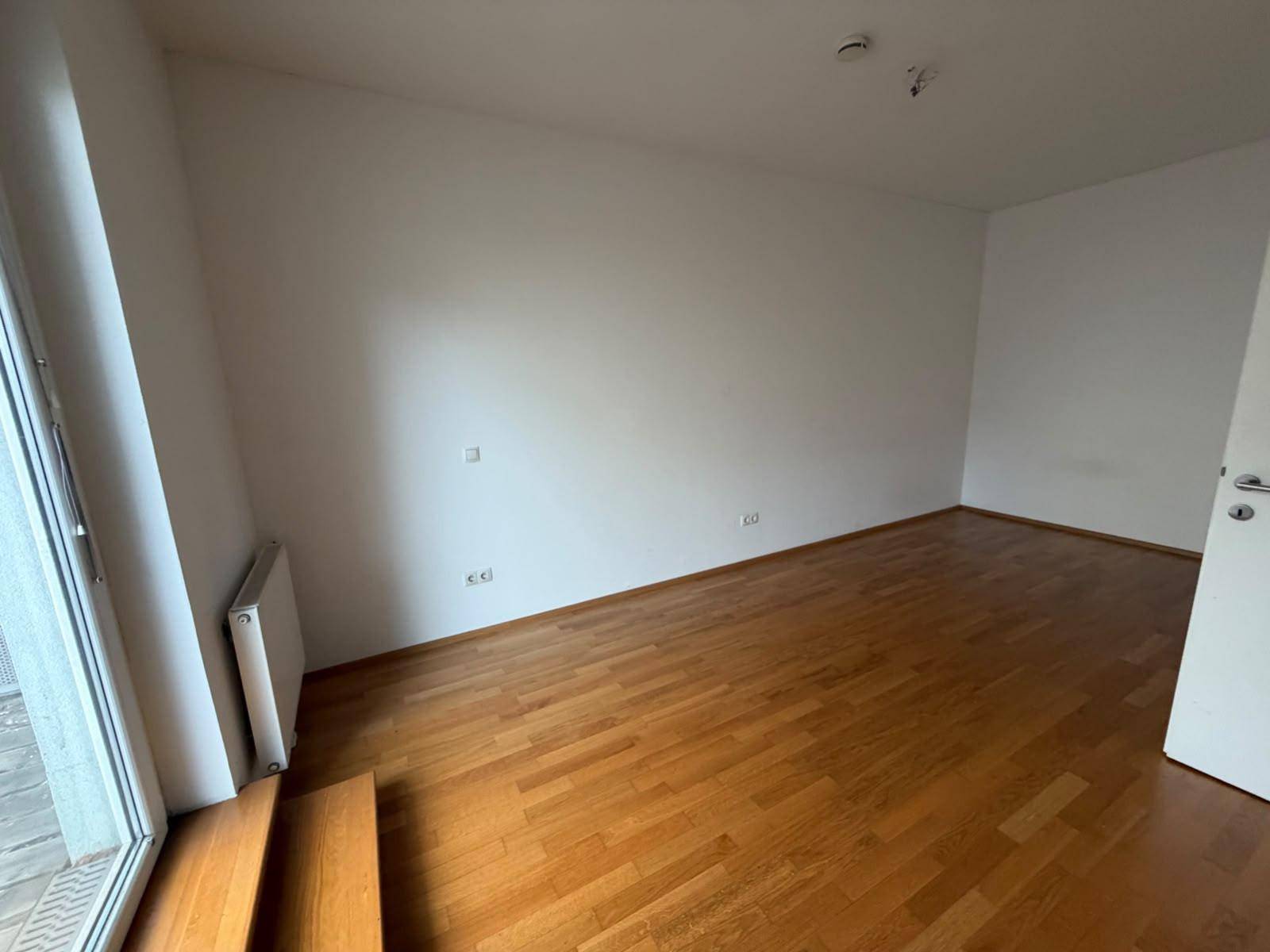 Leeres Zimmer mit Parkettboden und Fensterfront, die viel Tageslicht hereinlässt, vielseitig nutzbar.