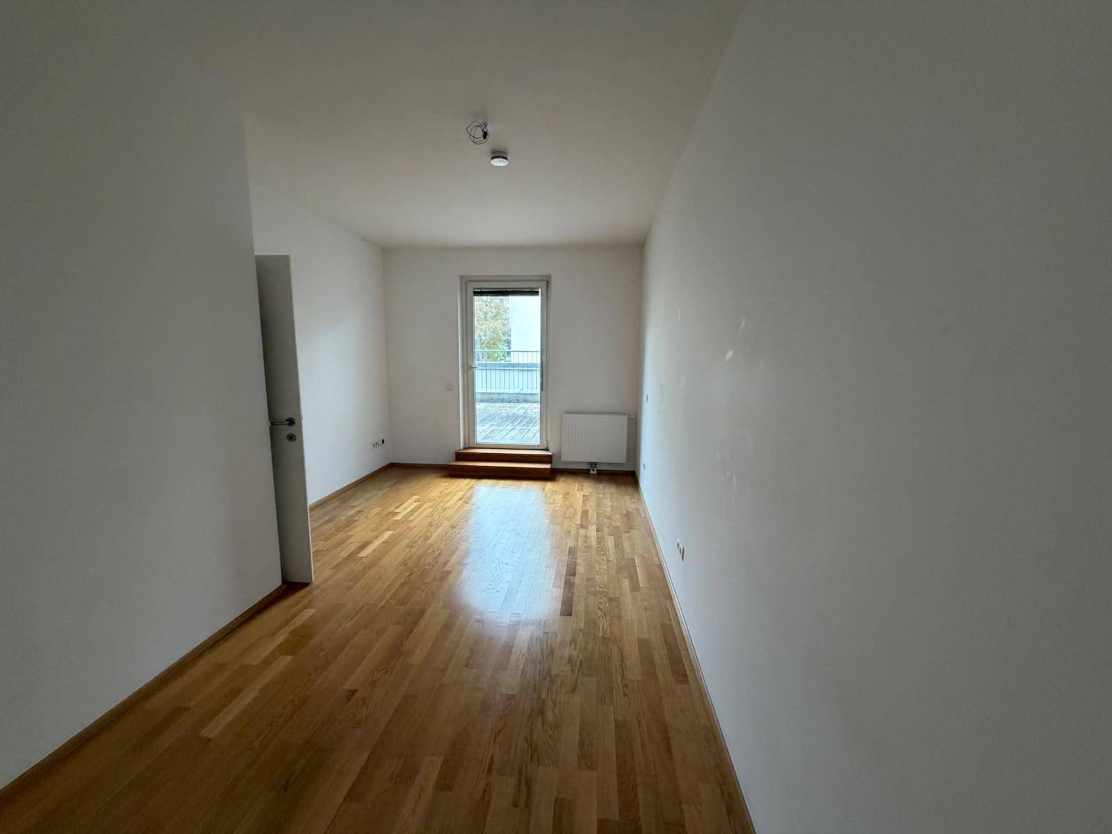 Langes, helles Zimmer mit Parkettboden und Zugang zu einem Außenbereich, bietet viel Platz.