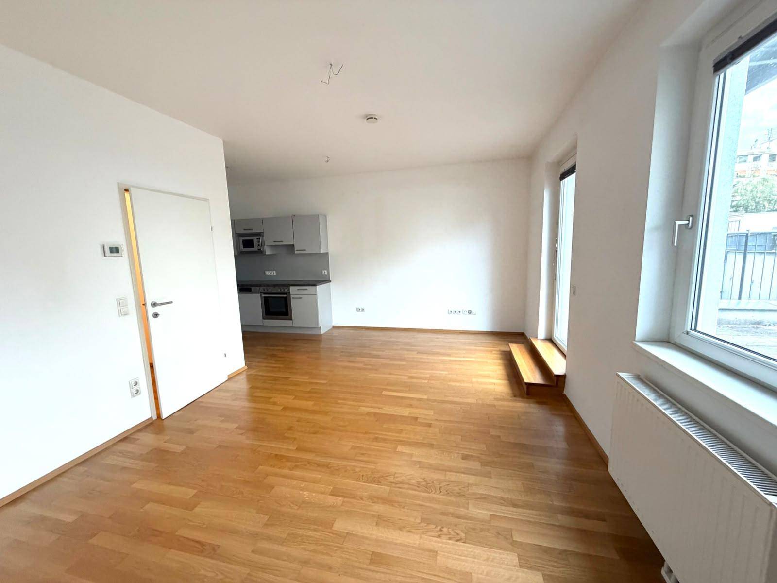 Heller Wohnbereich mit Parkettboden und offener Verbindung zur Küche im Hintergrund, ideal für modernes Wohnen.