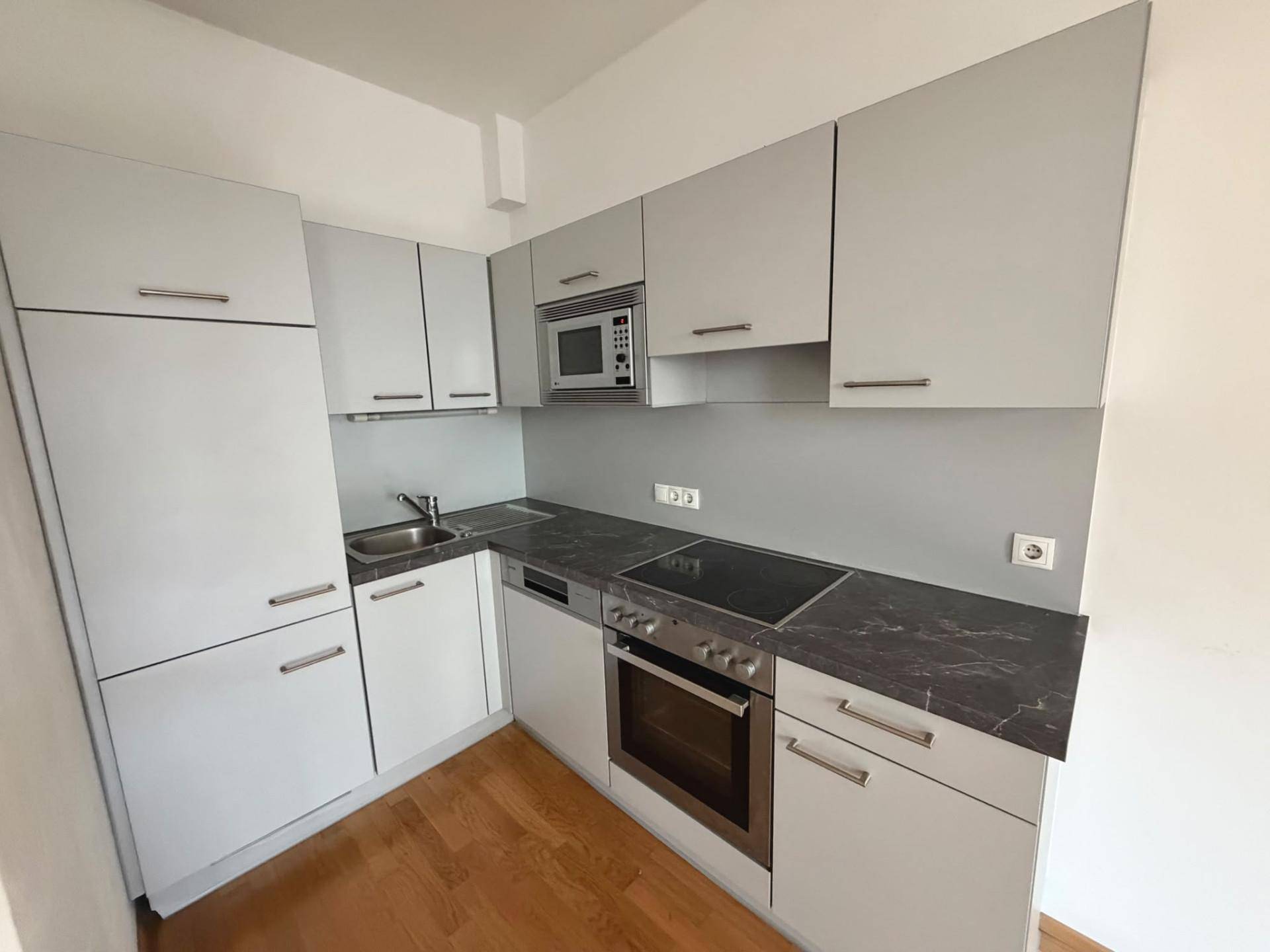 Moderne Einbauküche mit grauen Hochglanzfronten, dunkler Arbeitsplatte und integrierten Geräten.
