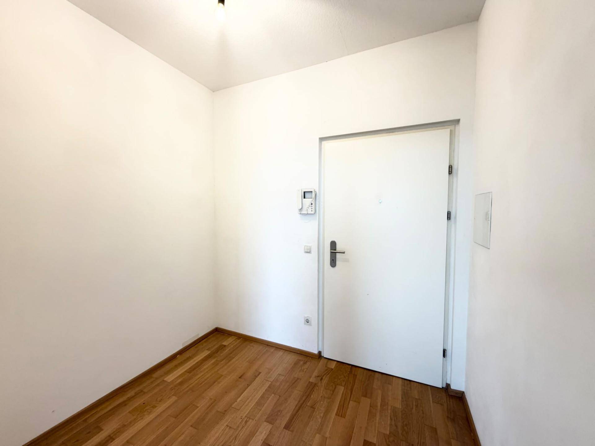 Heller Eingangsbereich mit Parkettboden und weißer Tür, die in die Wohnung führt, einladend gestaltet.