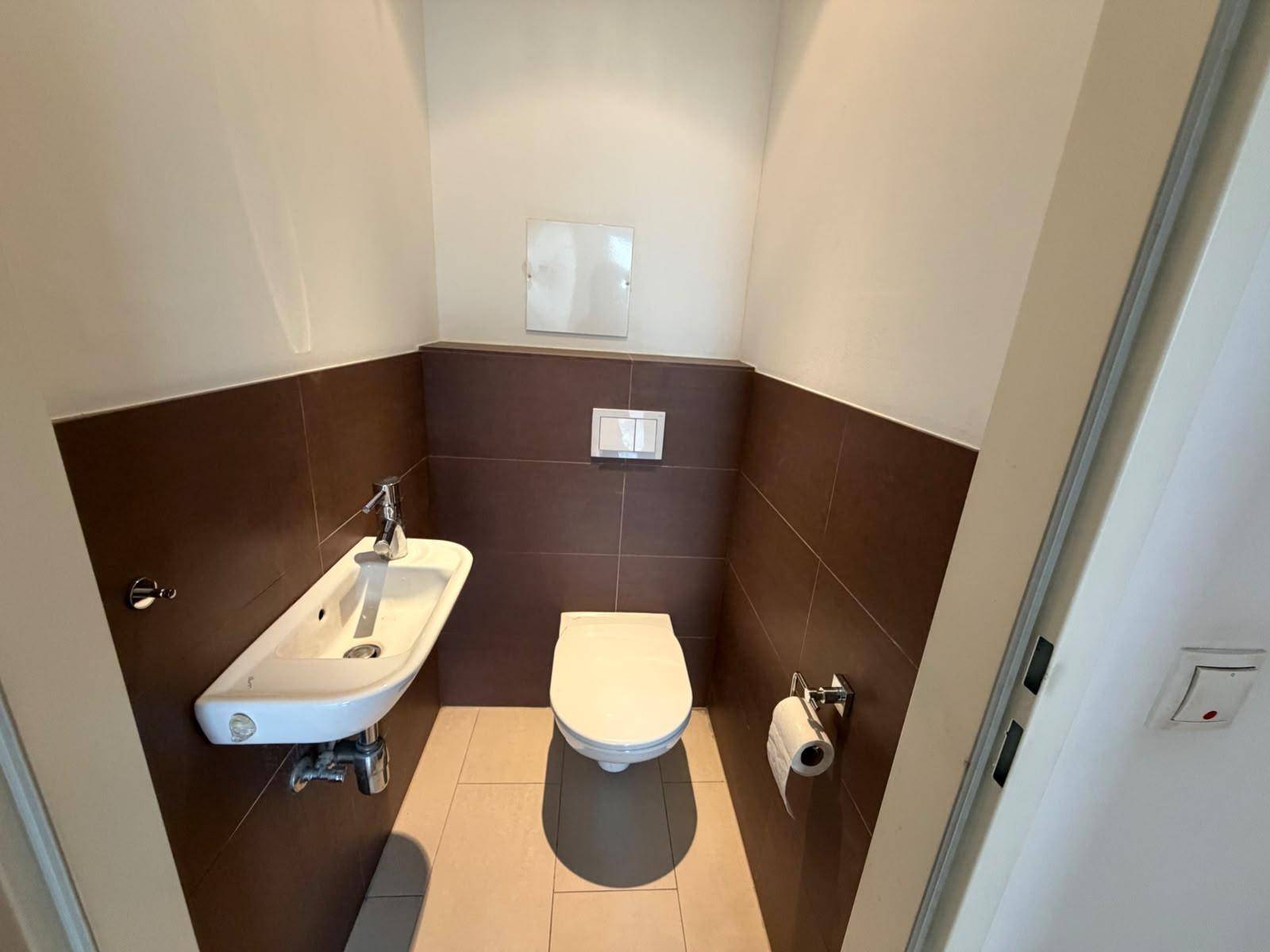 Separates WC mit Wand-WC und kleinem Handwaschbecken, modern gefliest und funktional.