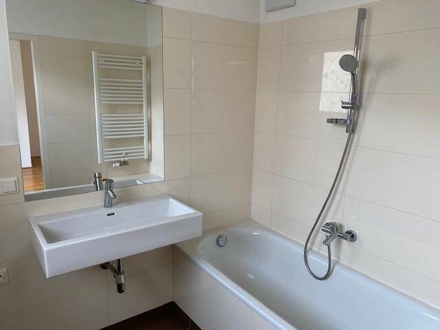 Modernes Badezimmer mit Badewanne, Waschbecken und beheiztem Handtuchhalter, hell gefliest.