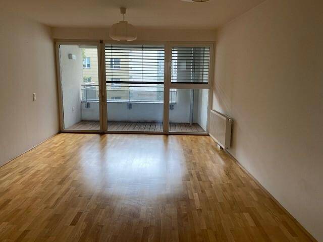 Heller Wohnraum mit Holzboden und großem Zugang zu einem Balkon, unmöbliert.
