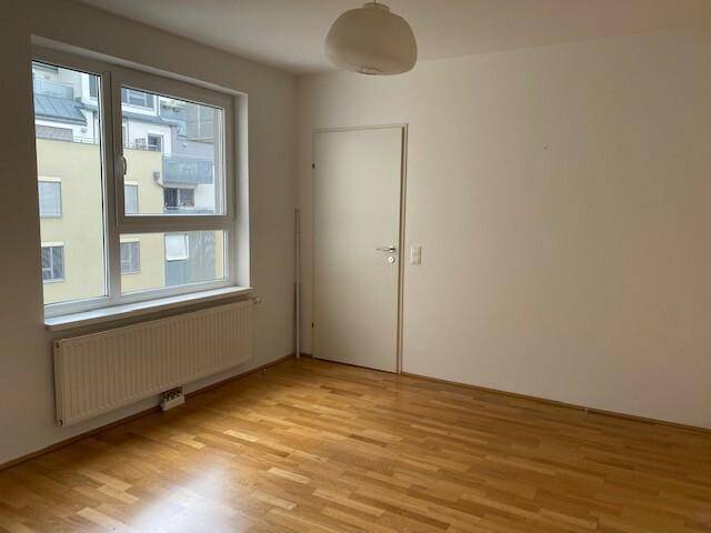 Helles, leeres Zimmer mit Holzboden und großem Fenster, ideal als Schlafzimmer.