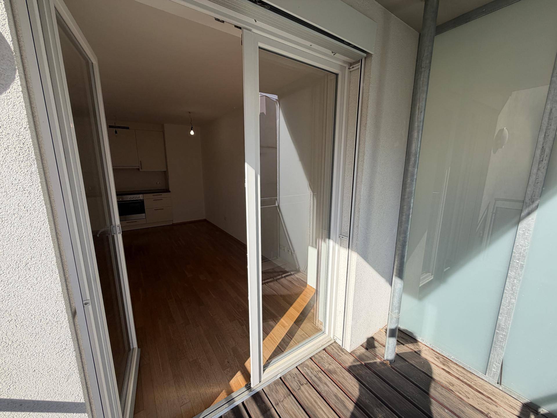 Blick vom Balkon in eine helle Küche mit Parkettboden und Einbauküche.